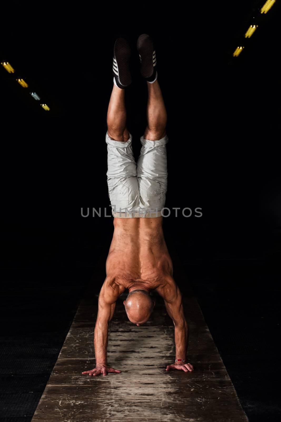 Senior man standing on hands upside down in dark gym