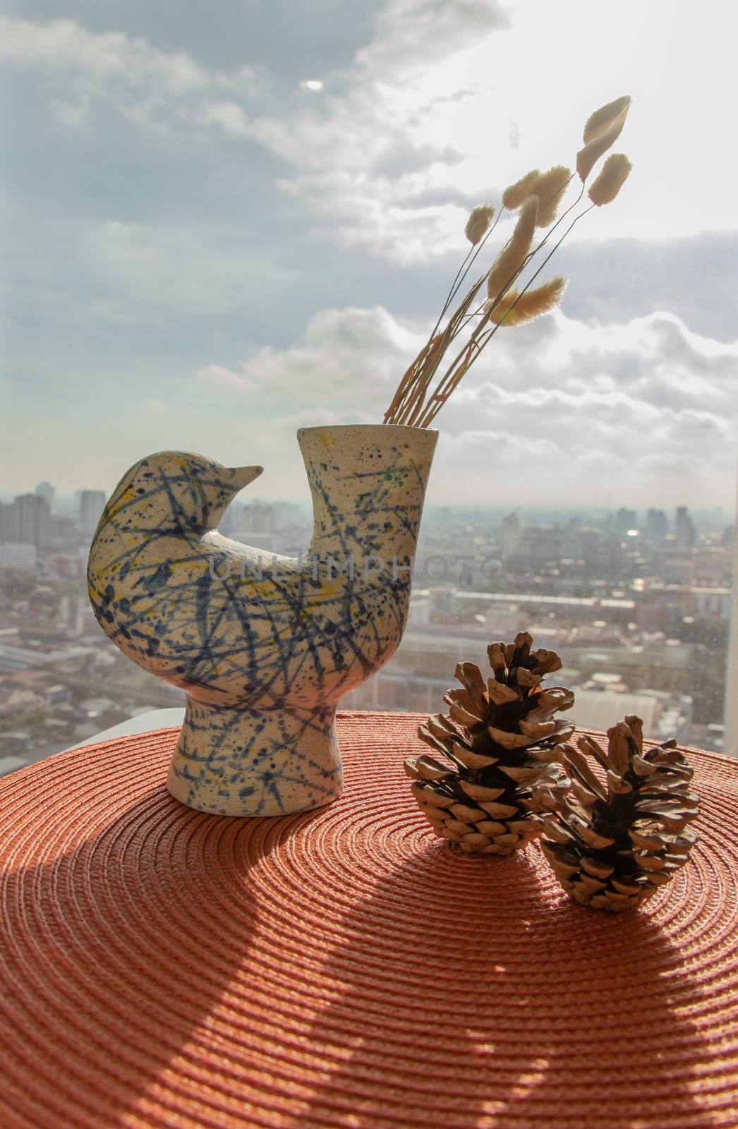 Dried flowers in beautiful ceramic blue vase handmade with two pine cones on table of living room and city view. Home decor. Space for text. Selective focus.