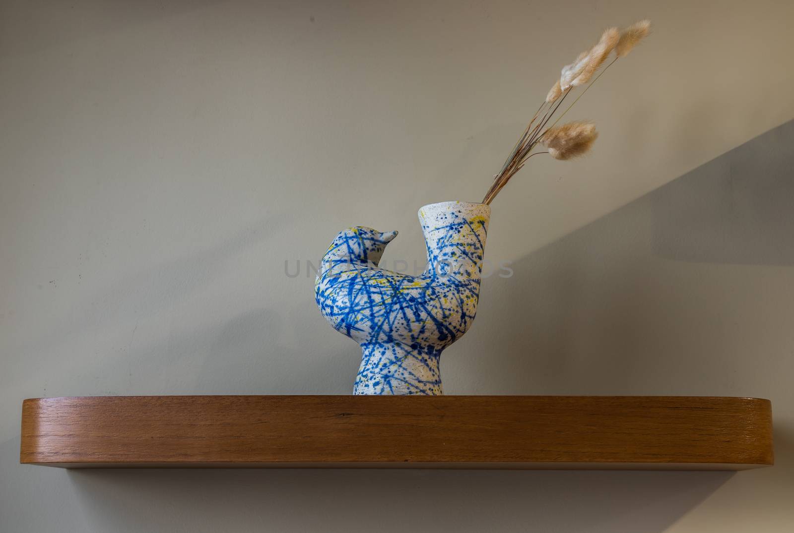 Dried flowers in beautiful ceramic blue vase standing on wooden shelf on wall of living room. Home decor. Space for text. Selective focus.