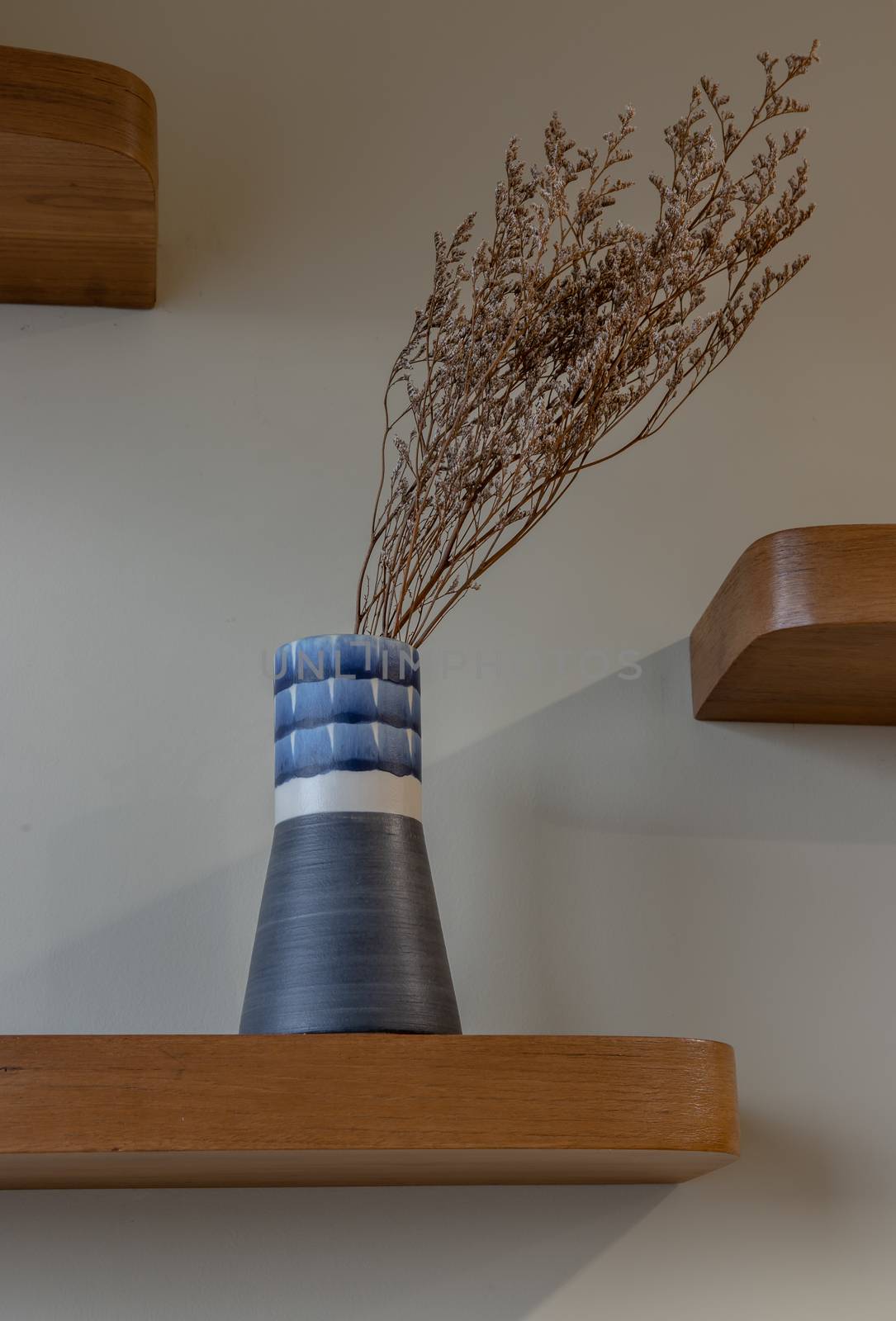 Dried flowers in beautiful ceramic blue vase standing on wooden shelf on wall of living room. Home decor. Space for text. Selective focus.
