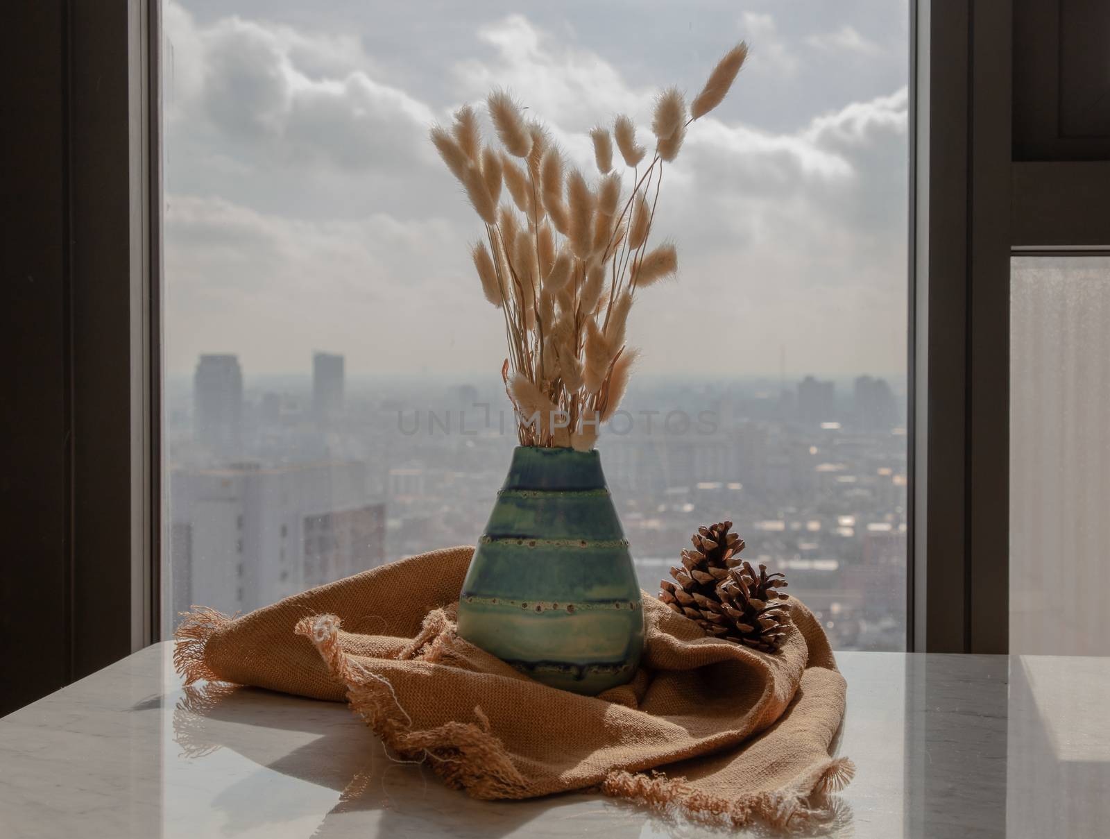 Dried flowers in beautiful ceramic blue vase handmade with two pine cones on marble table of living room and city view. Home decor. Space for text. Selective focus.