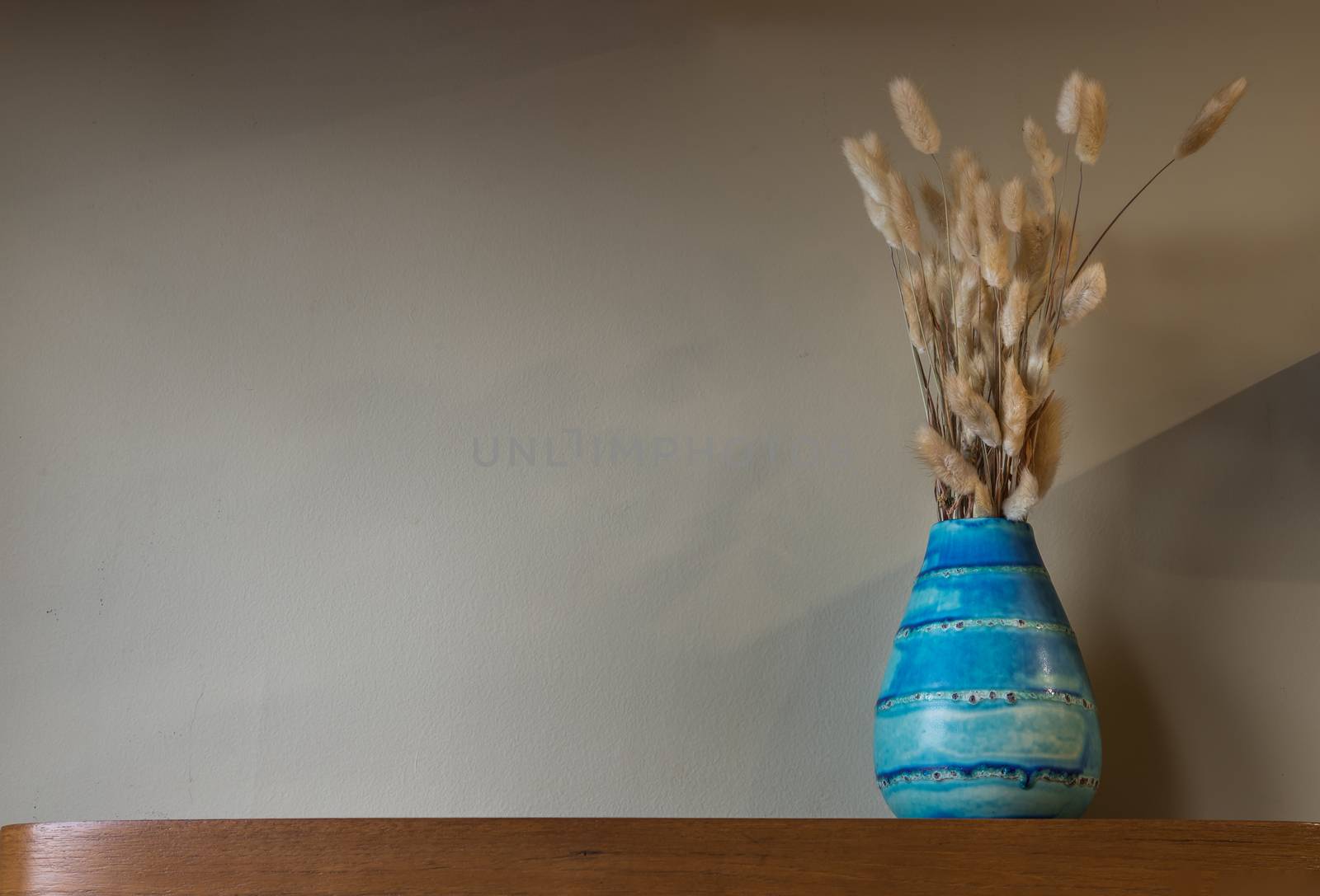 Dried flowers in beautiful ceramic blue vase standing on wooden shelf on wall of living room. Home decor. Space for text. Selective focus.