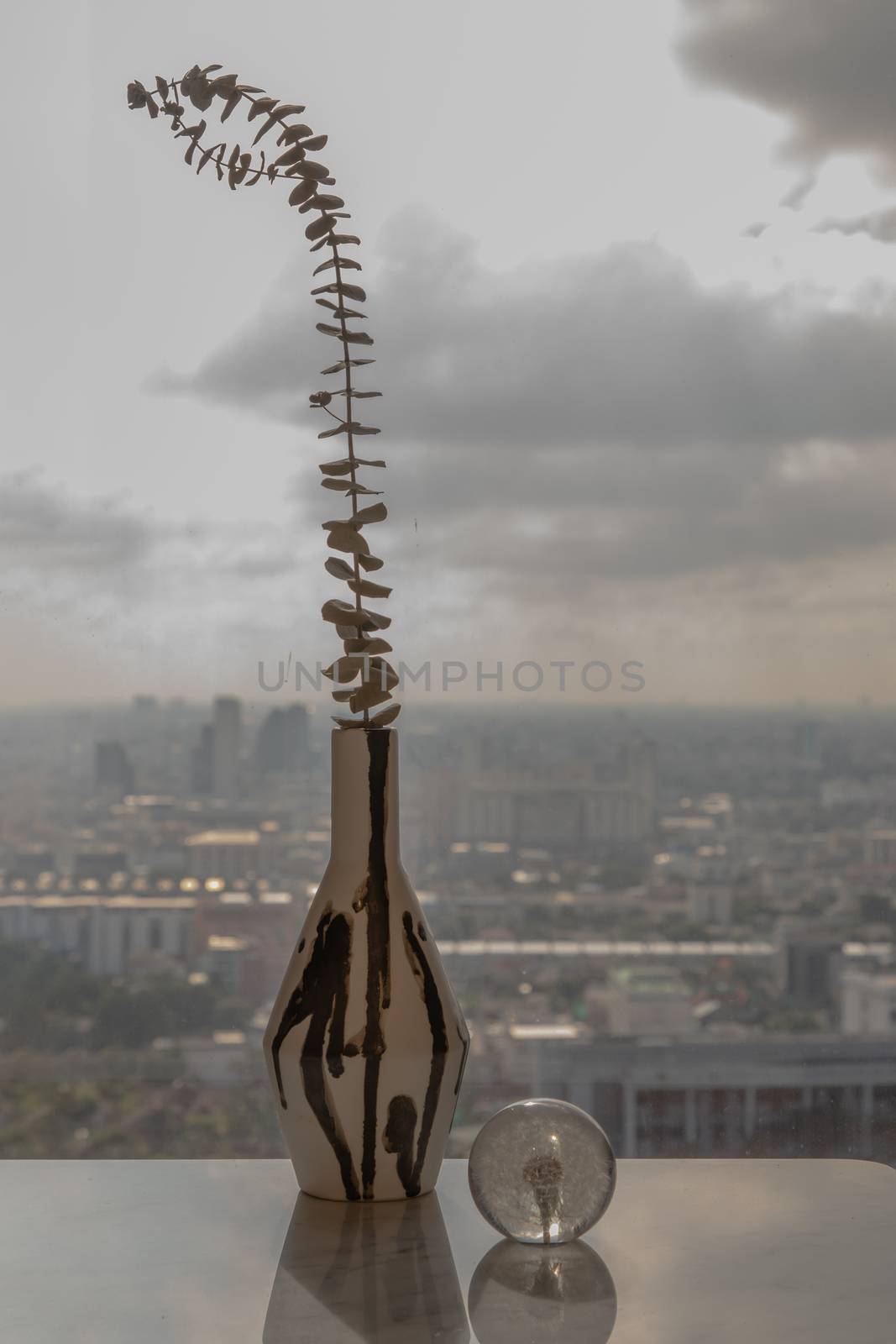 Dried flowers in beautiful ceramic black and white vase handmade with glass paper weight on marble table of living room and city view. Home decor. Space for text. Selective focus.