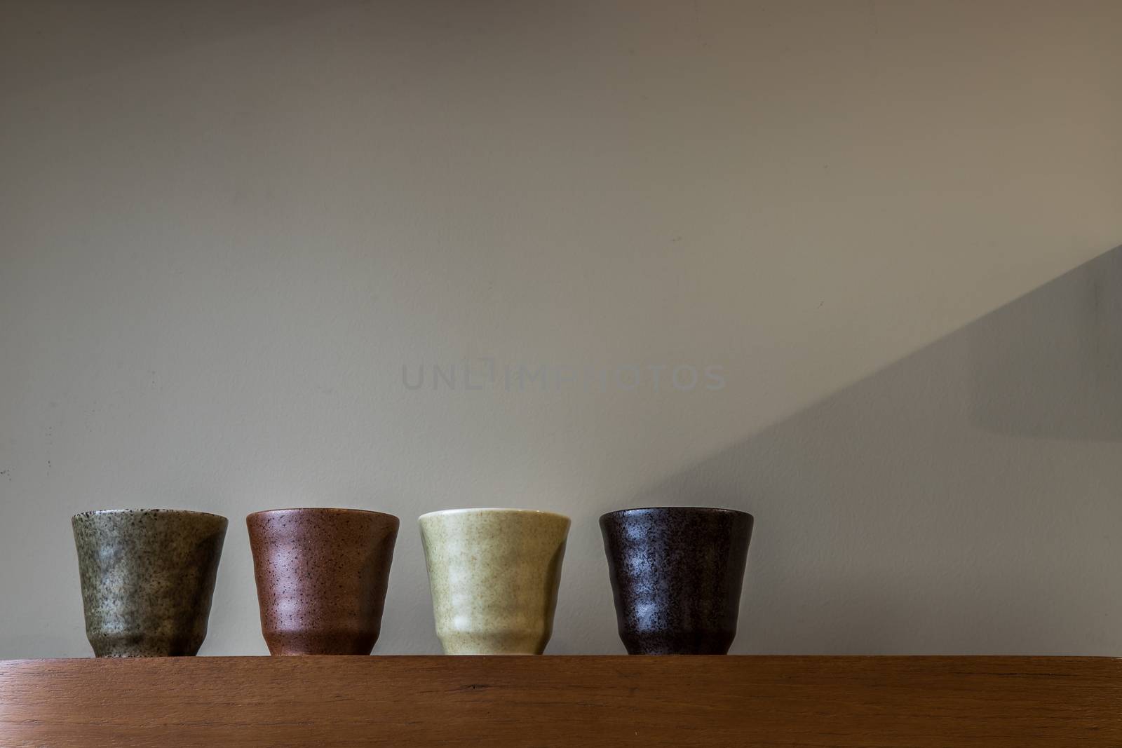 Four ceramics mugs handmade on the wooden shelf on wall of living room. Home decor. Space for text. No focus, specifically.