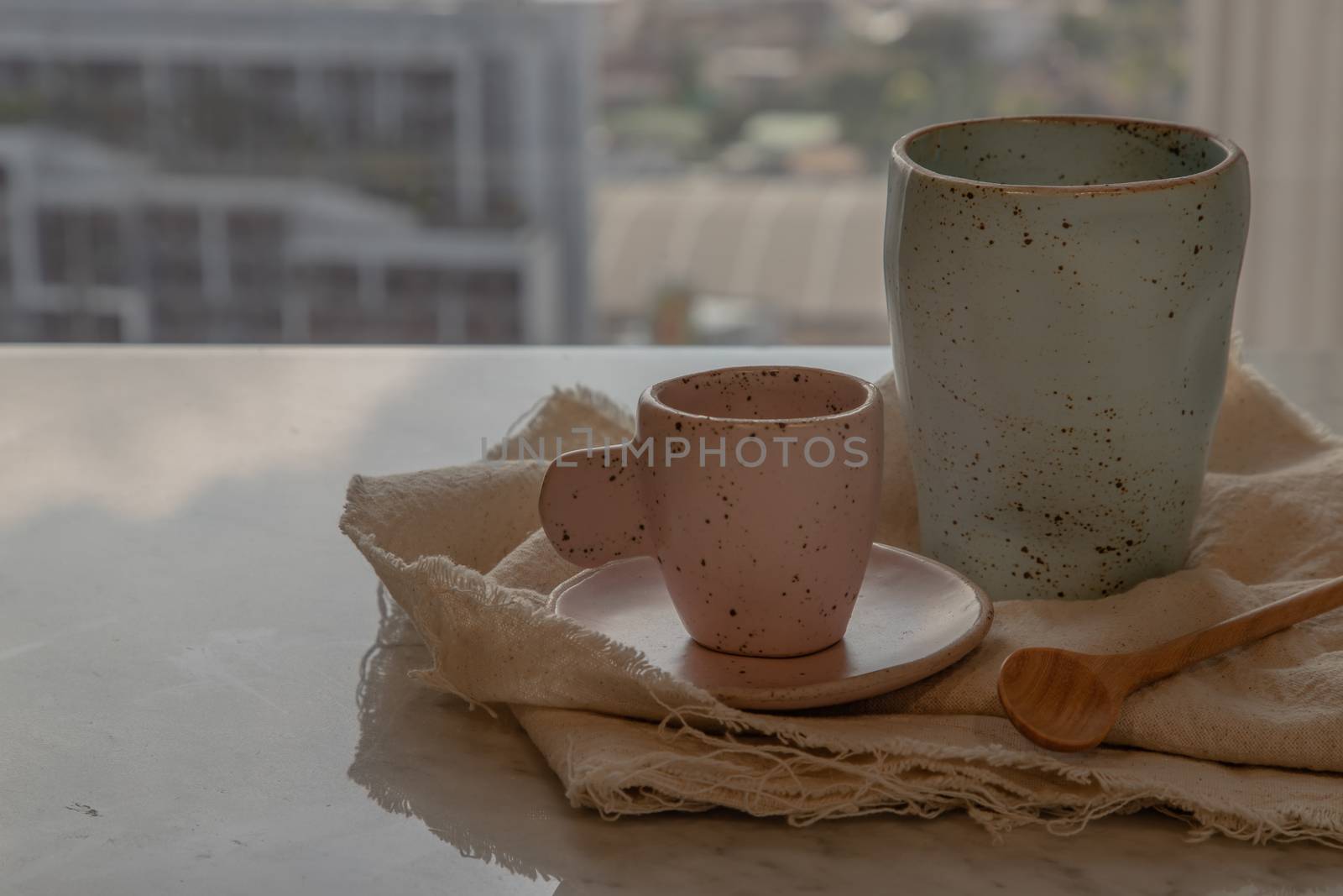 Blue and pink ceramics mugs handmade with wooden spoon on marble table of living room and city view. Home decor. Space for text. No focus, specifically.