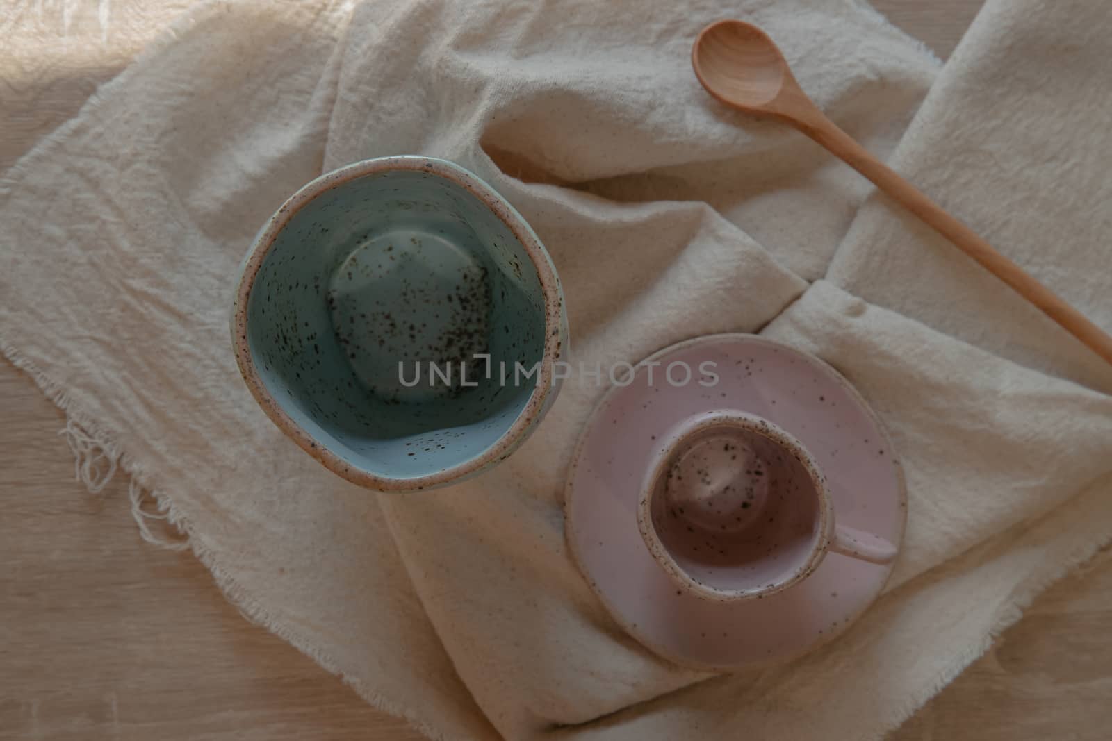 Blue and pink ceramics mugs handmade with wooden spoon on white calico. Home decor. Space for text. No focus, specifically.