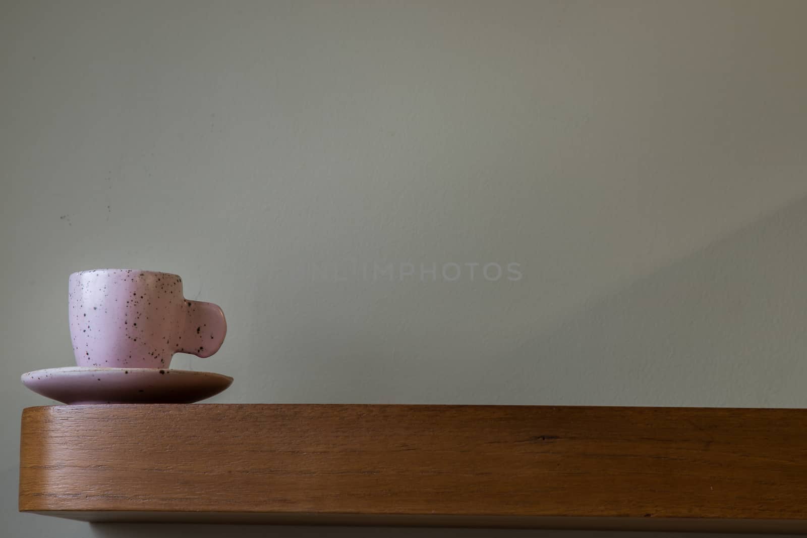 Pink ceramic mug handmade on the wooden shelf on wall of living room. Home decor. Space for text. Selective focus.