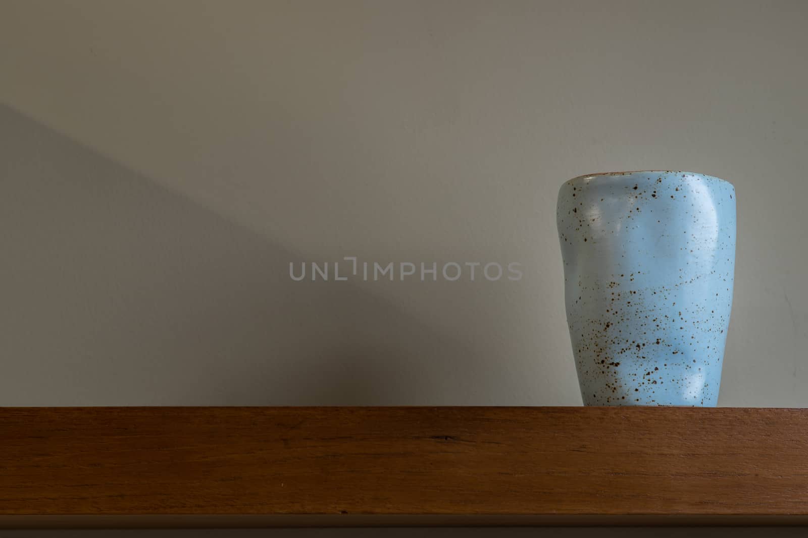 Blue ceramic mug handmade on the wooden shelf on wall of living room. Home decor. Space for text. Selective focus.