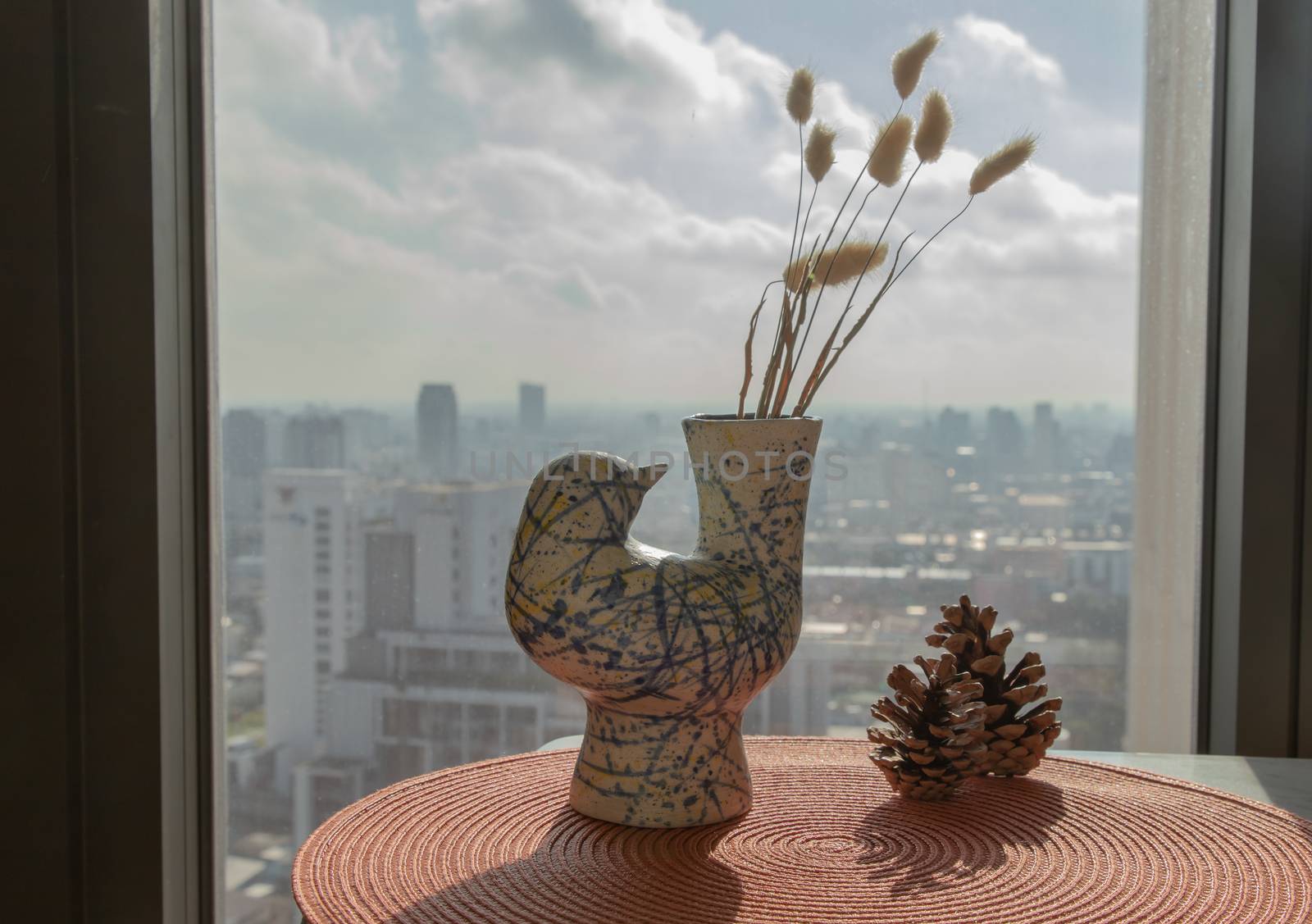 Dried flowers in beautiful ceramic blue vase handmade with two pine cones on table of living room and city view. Home decor. Space for text. Selective focus.