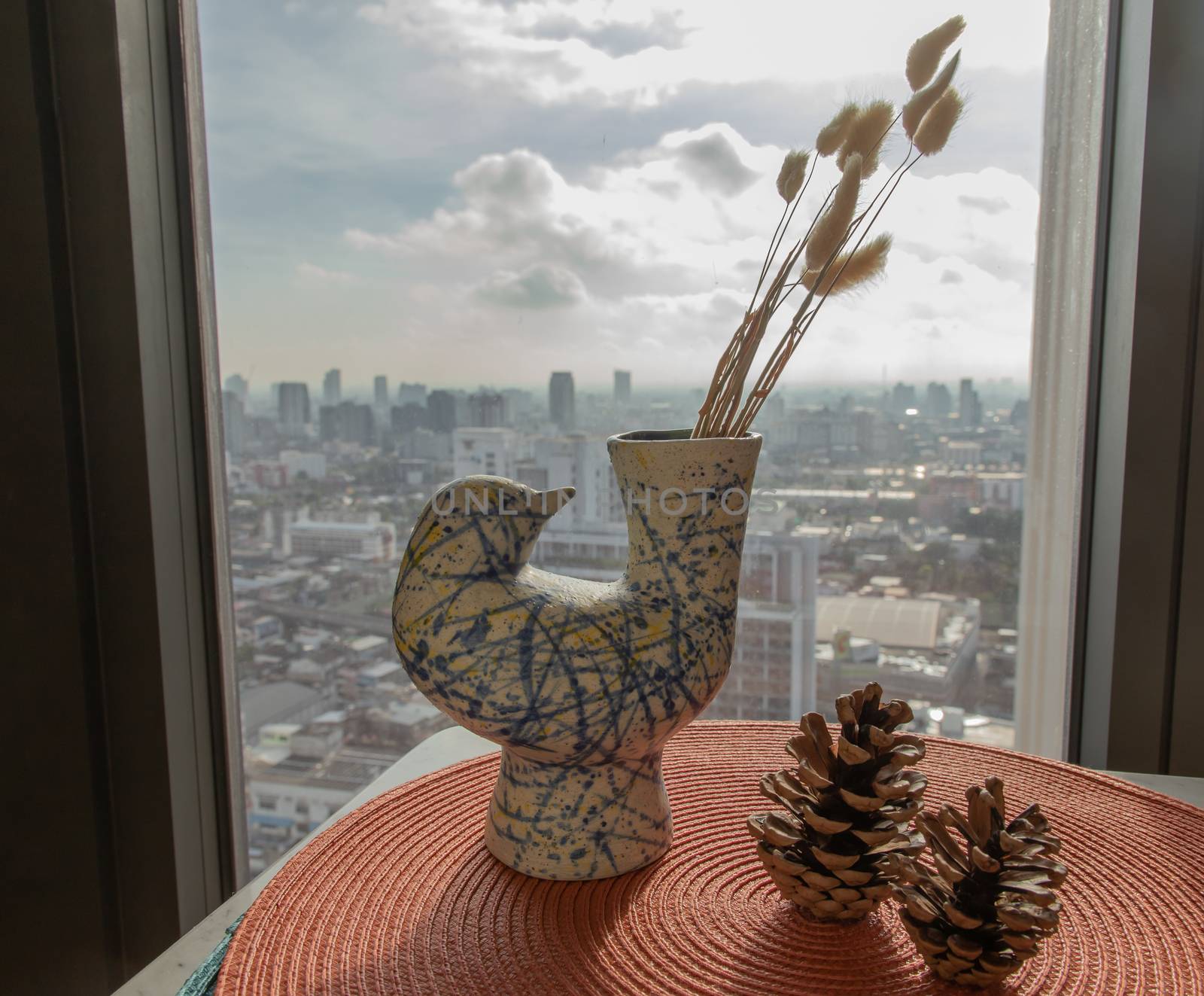 Dried flowers in beautiful ceramic blue vase handmade with two pine cones on table of living room and city view. Home decor. Space for text. Selective focus.