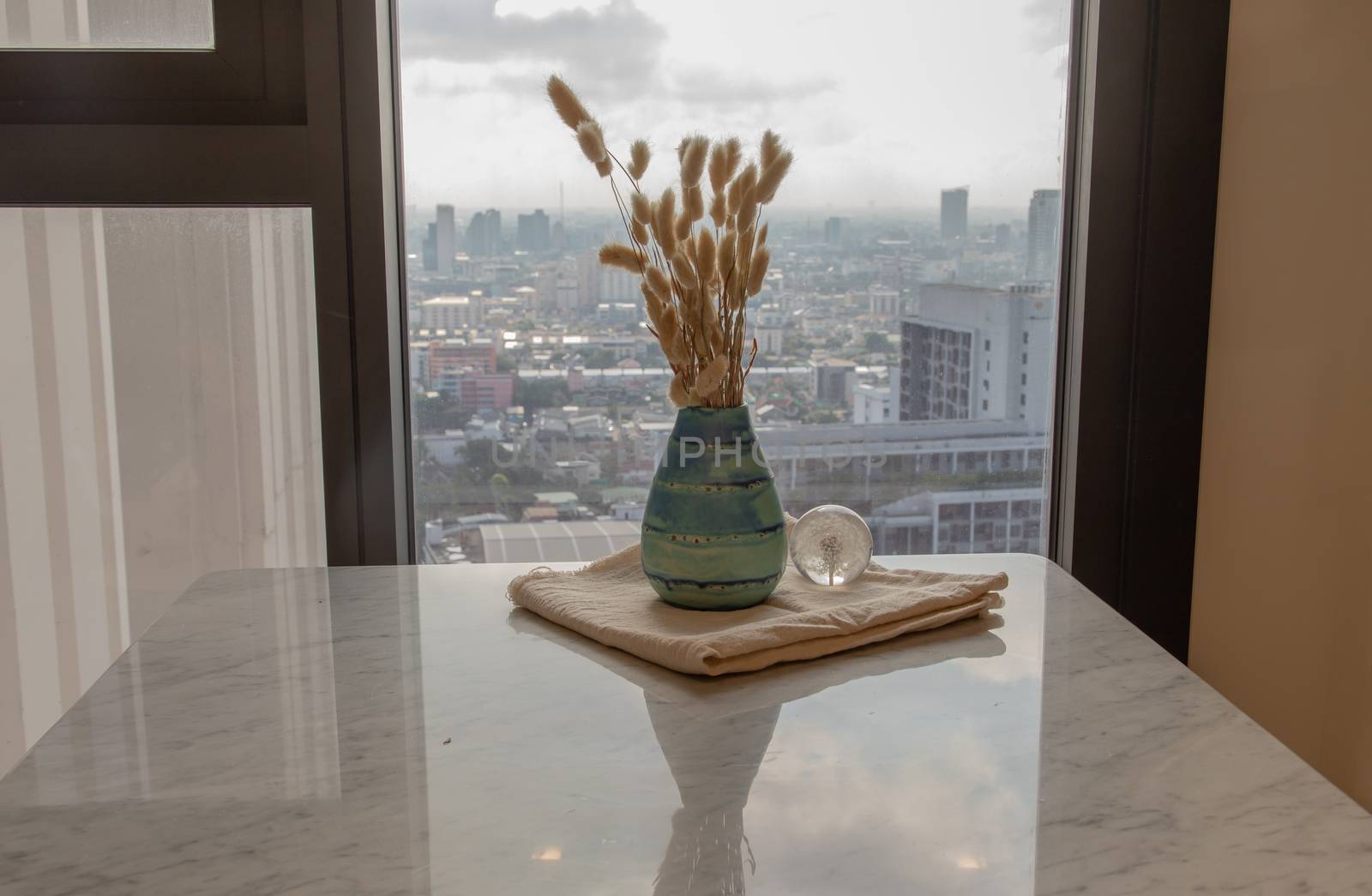 Dried flowers in beautiful ceramic blue vase handmade with glass paper weight on marble table of living room and city view. Home decor. Space for text. Selective focus.