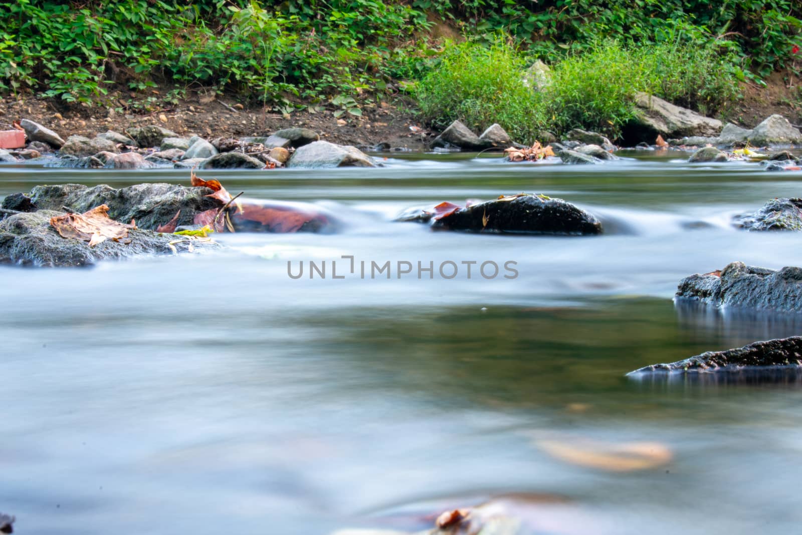 A Low Angle Long Exposure Of a Stream Full of Multicolored Rocks by bju12290