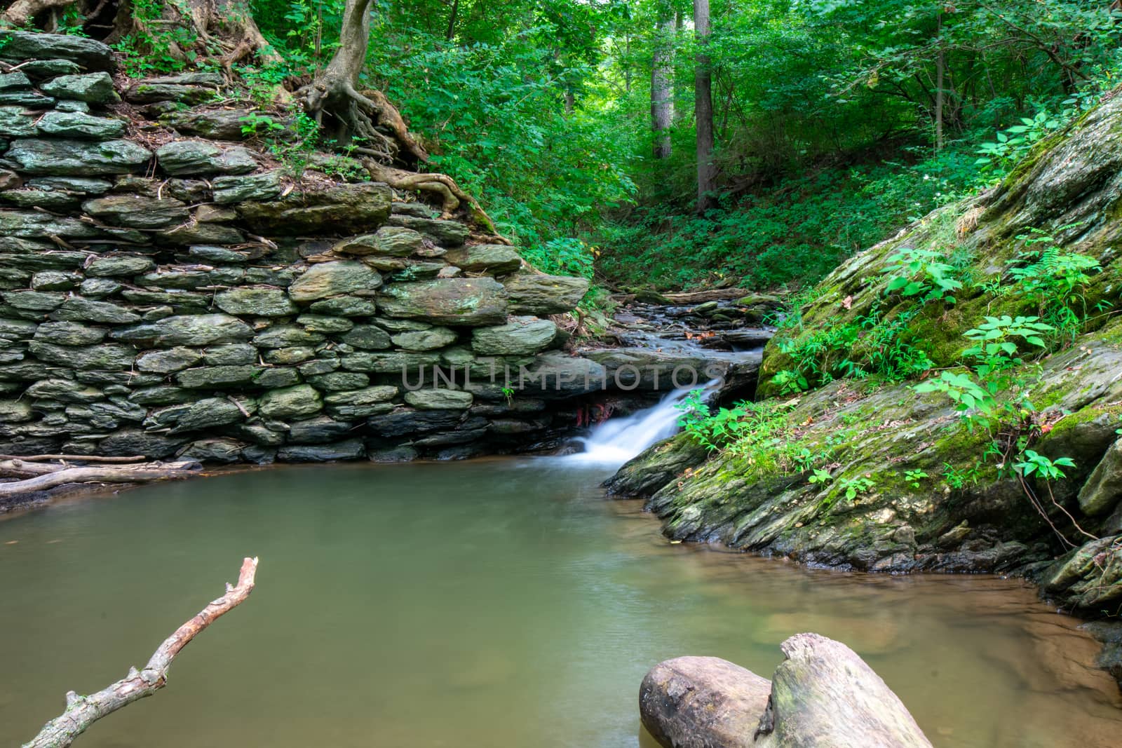 A Long Exposure of a Stream of Water Flowing Into a Small Body of Water Next to a Cobblestone Wall