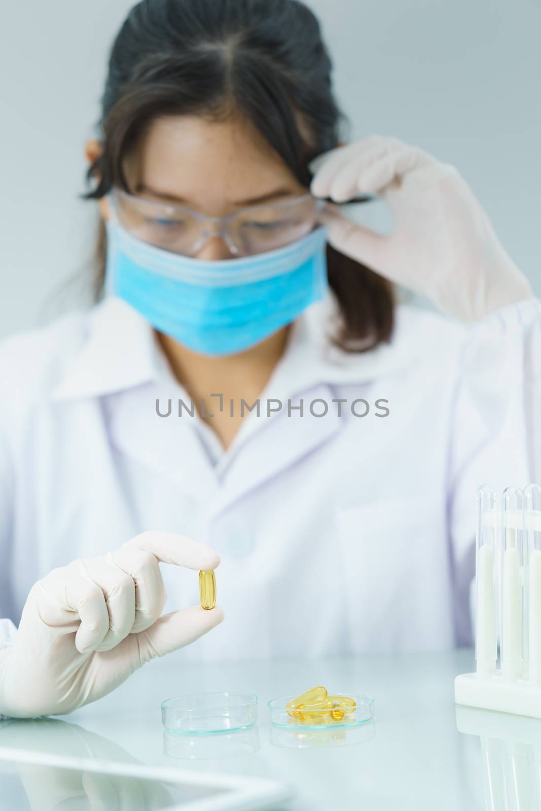 Close up Scientist hands putting in nitrile latex gloves holding Omega 3 capsule in labcoat doing experiments in lab