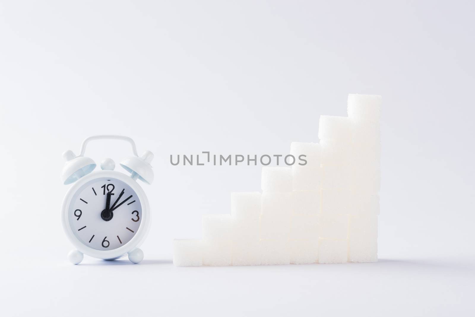 Ascending stacks of sugar cubes graph chart and alarm clock, studio shot isolated on white background, health high blood risk of diabetes concept