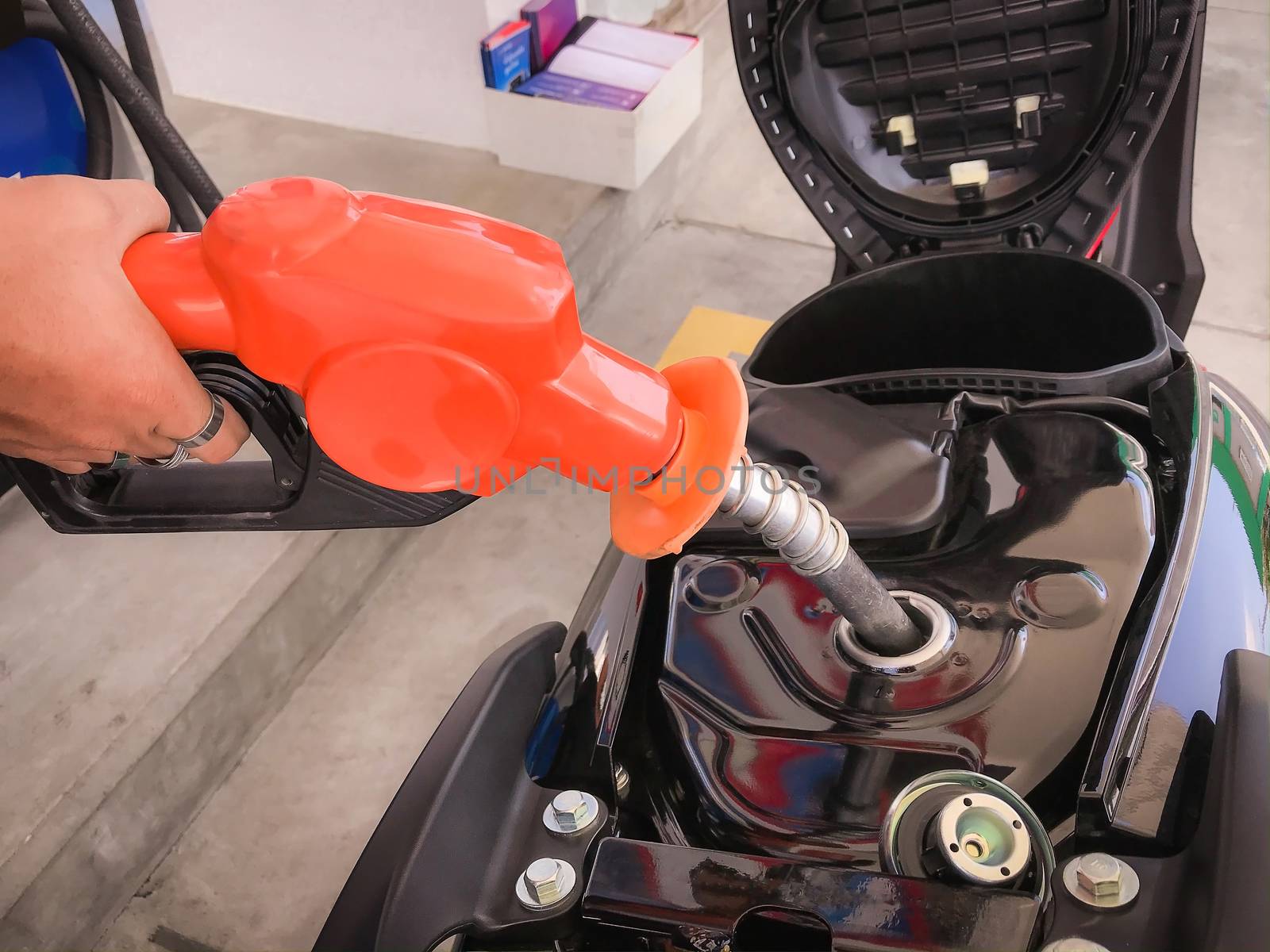 Closeup of the hand of the employee holding the fuel dispenser and adding benzyl fuel to the motorcycle's fuel tank.