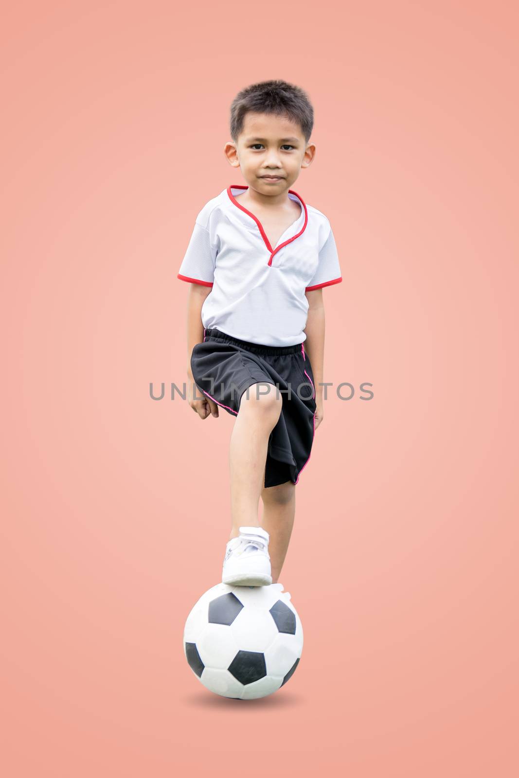 The boy in sportswear wearing sneakers is stepping on a soccer ball isolated on pastel color background, with clipping path.