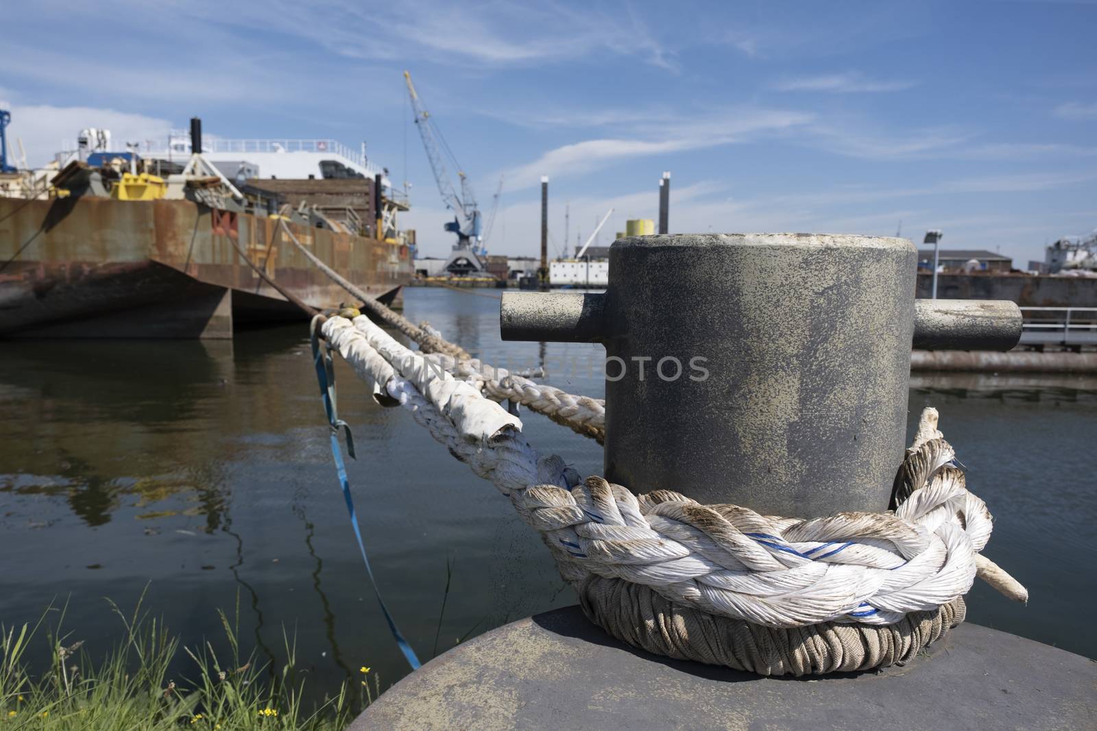 Rusty mooring bollard with ship ropes. Bollard with mooring ropes on the quay. Moored ship at the port quay in the Netherlands