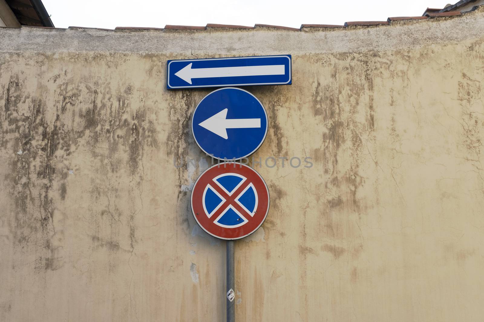 Old blue metallic arrow sign against a damaged concrete wall indicating to go left and no parking sign - concept image