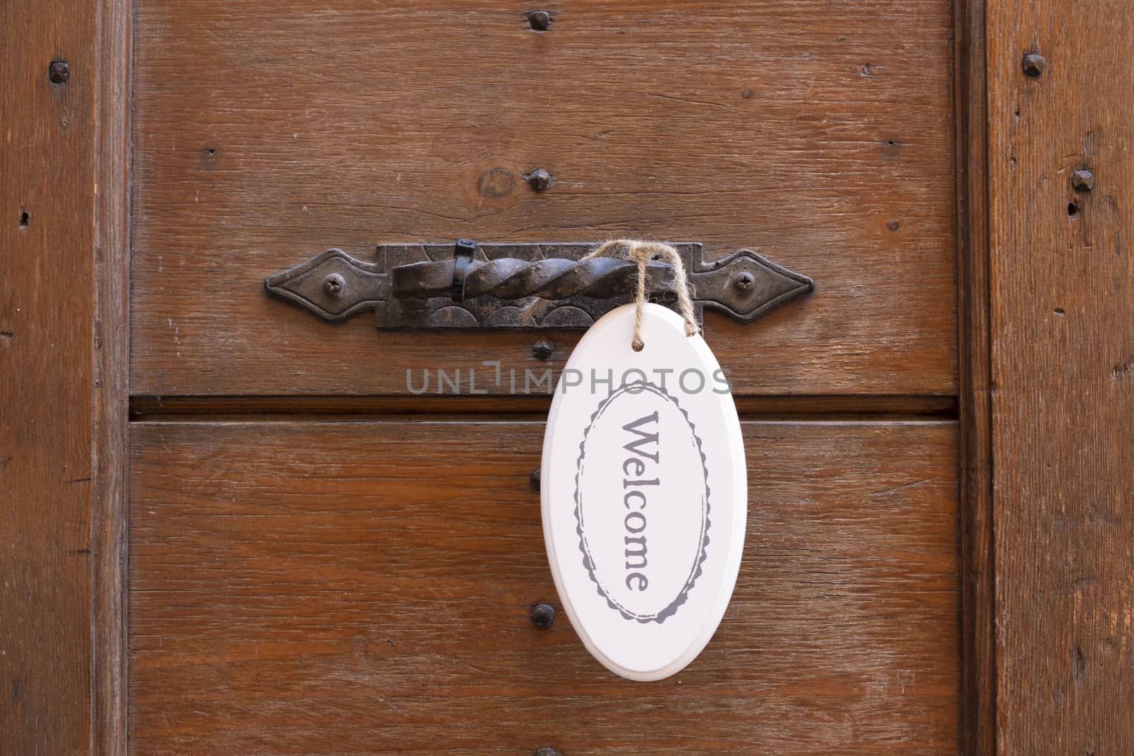 Antique door handle on a wooden door wit a welcome sign.