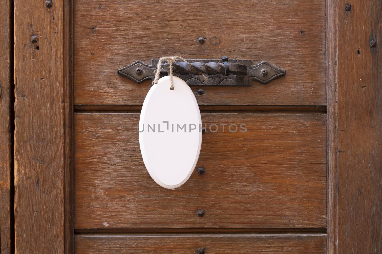 Antique door handle on a wooden door with a white sign hanging on a door by Tjeerdkruse