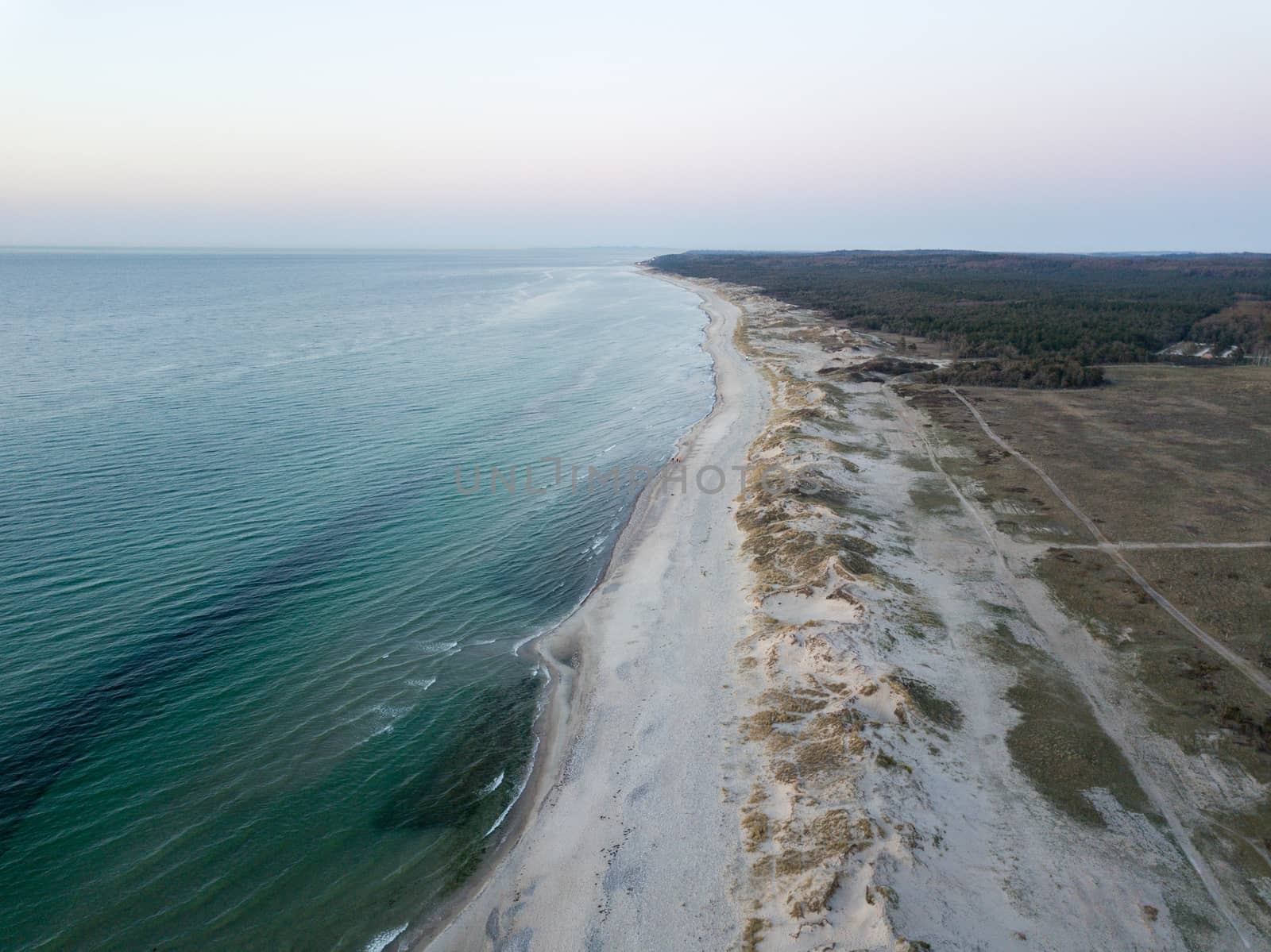 Melby, Denmark - April 18, 2019: Aerial drone view of the coastline beach, sand dunes and forest during sunset.