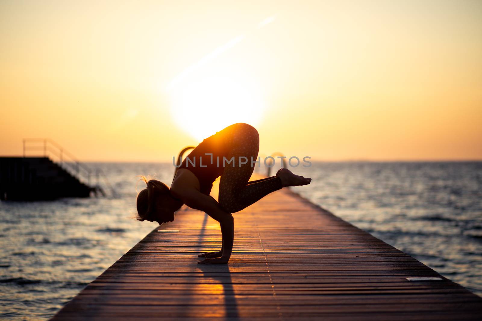 Silhouette of a woman practizing yoga on a wooden pier during sunset.
