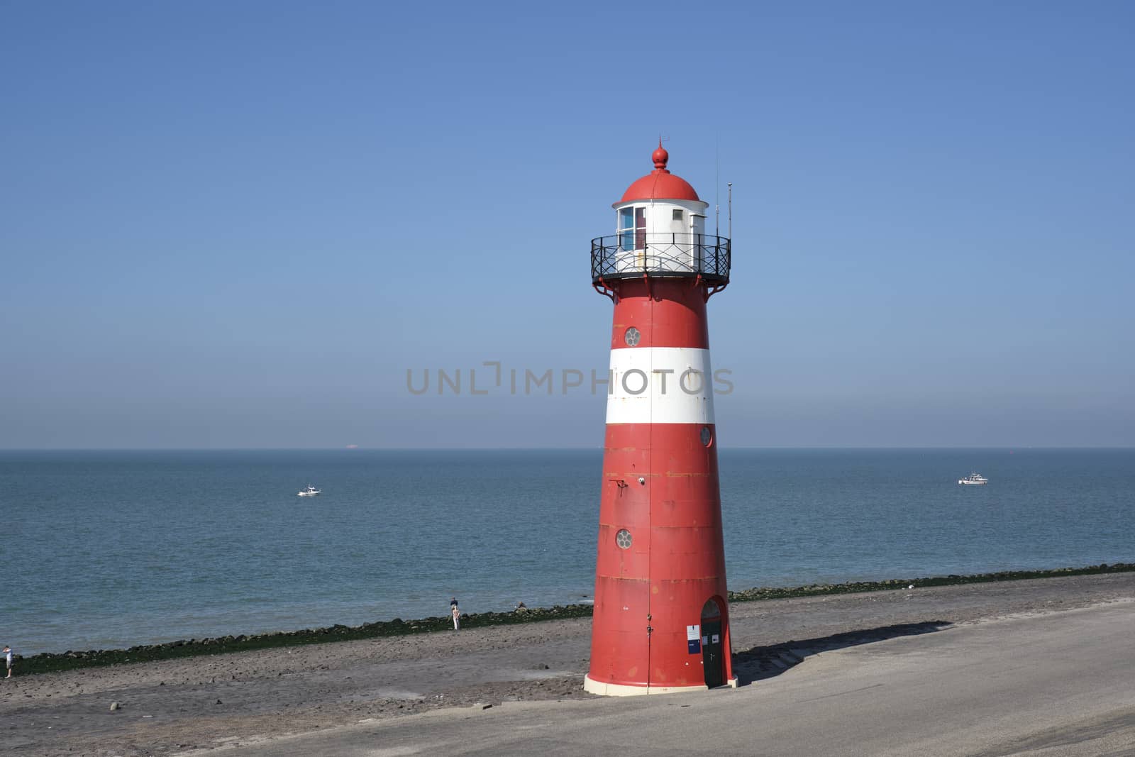 Red and white lighthouse on a blue sky background, Westkapelle, The Netherlands by Tjeerdkruse