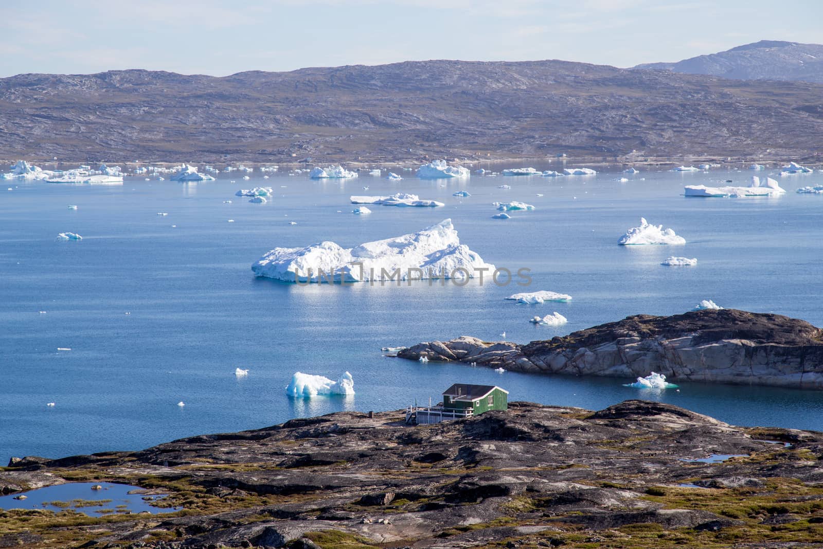 Ilulissat, Greenland - July 08, 2018: A green wooden house at the coast with icebergs in the background.