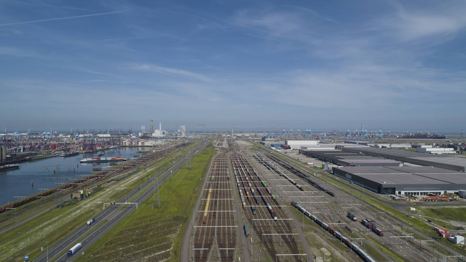 Aerial bird view photo of railroad container terminal with train loaded with containers by overhead crane also showing classification yard and heavy industry in background