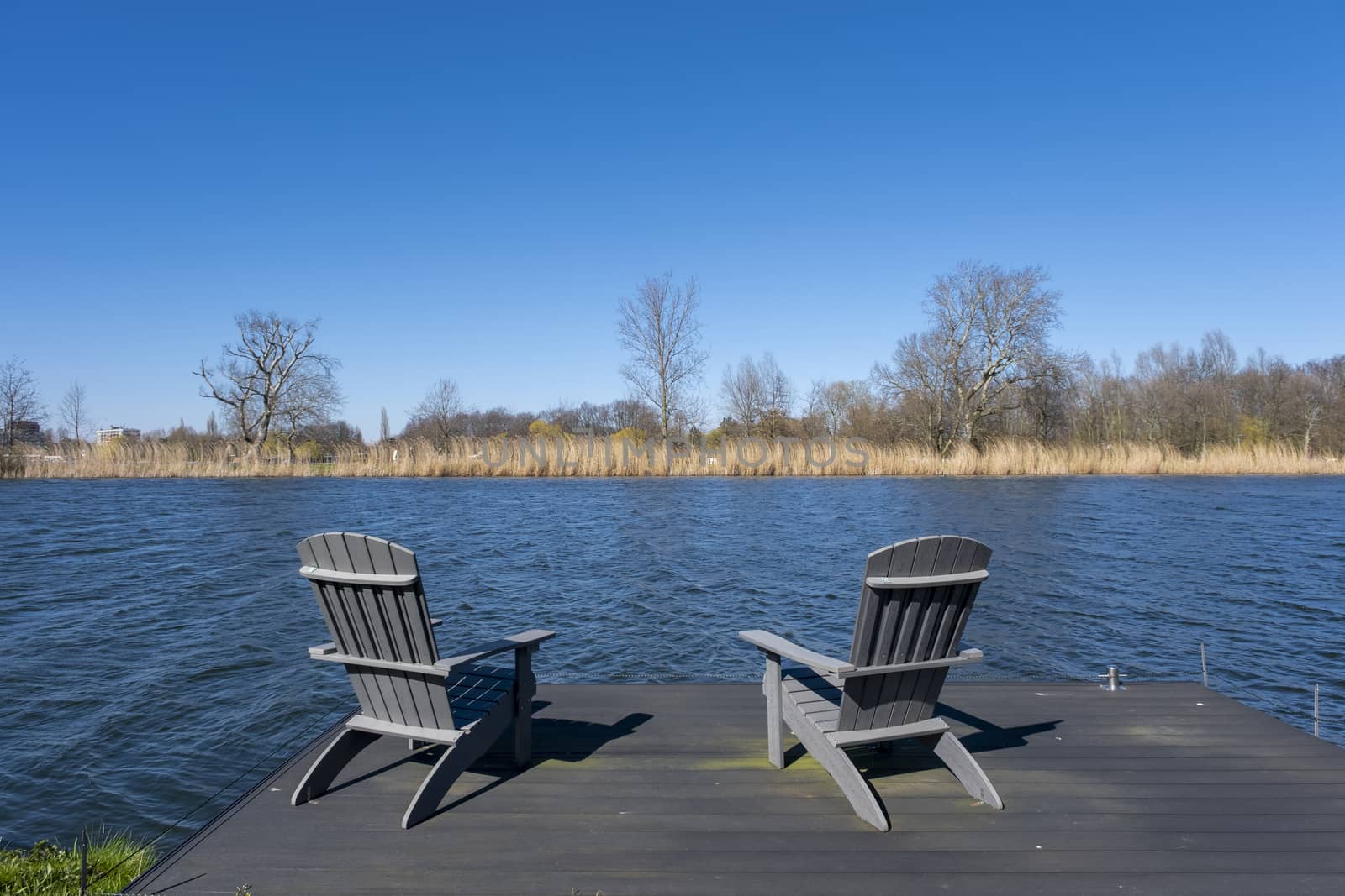 Rustic hand crafted chairs on a wooden deck overlooking a river  by Tjeerdkruse