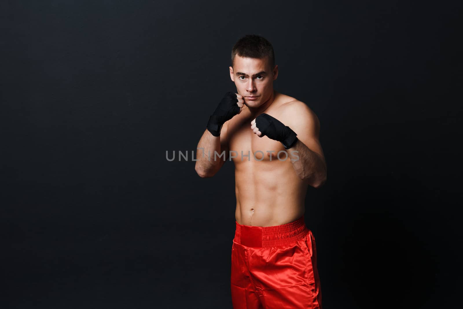 Sportsman muay thai man boxer stance in red truncks at black background by primipil