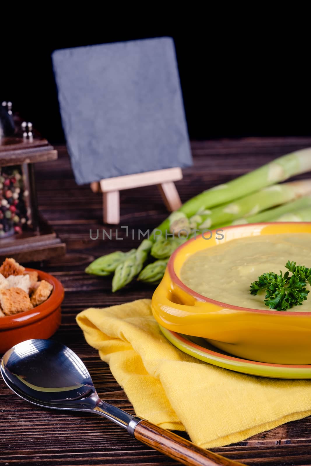 Fresh asparagus creamy soup and ingredients on wooden table on rustic wooden background, selective focus