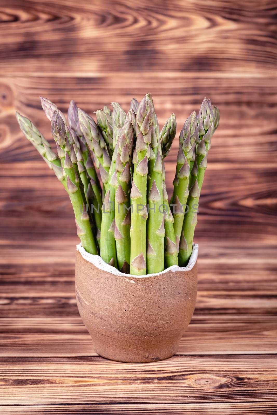 Asparagus in earthen bowl on rustic wooden background by Fischeron