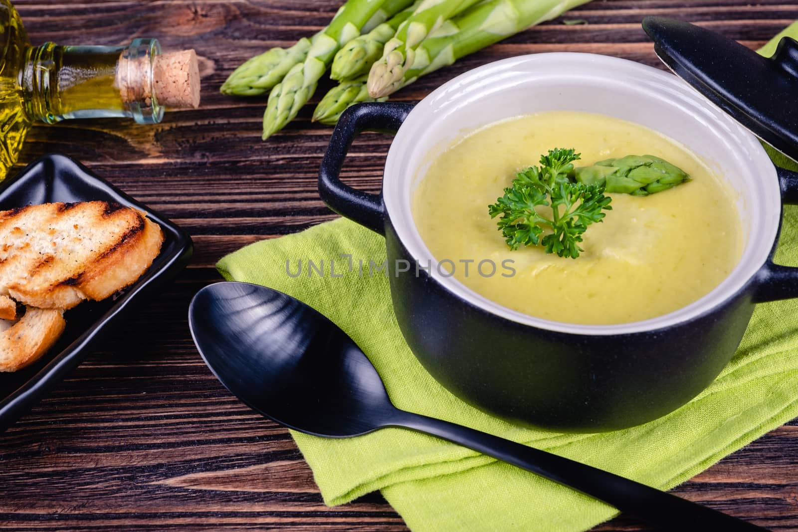 Fresh asparagus creamy soup and ingredients on wooden table on rustic wooden background, selective focus