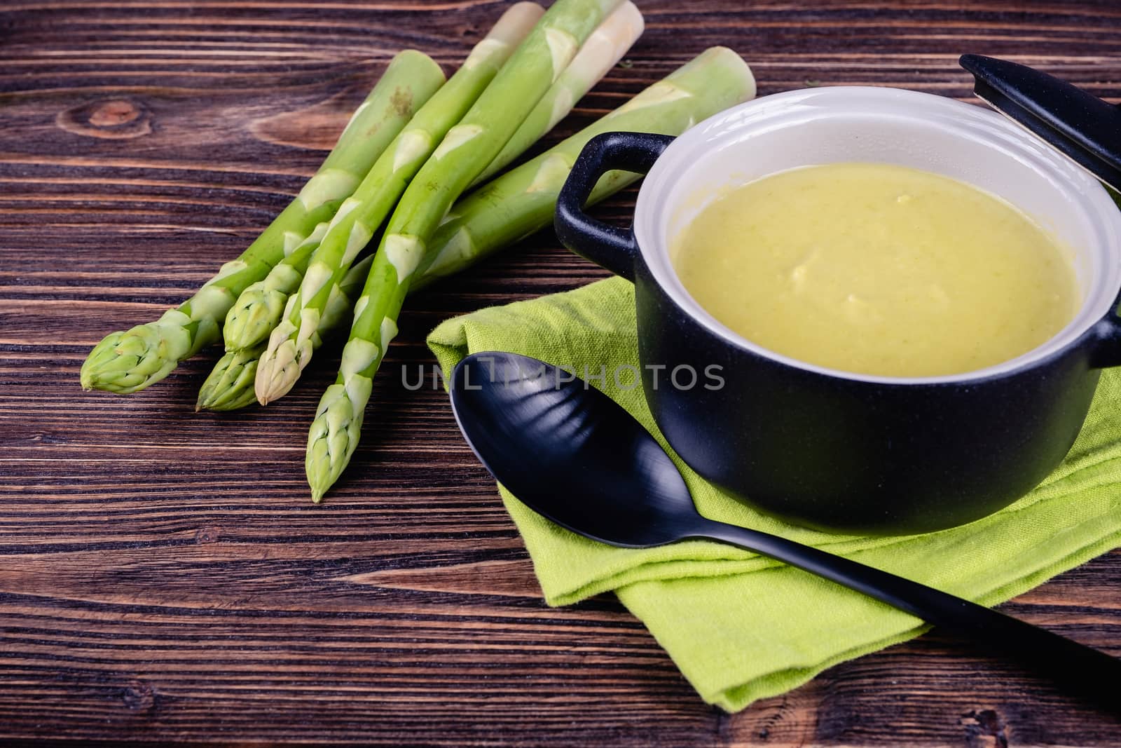 Fresh asparagus creamy soup and ingredients on wooden table on rustic wooden background, selective focus