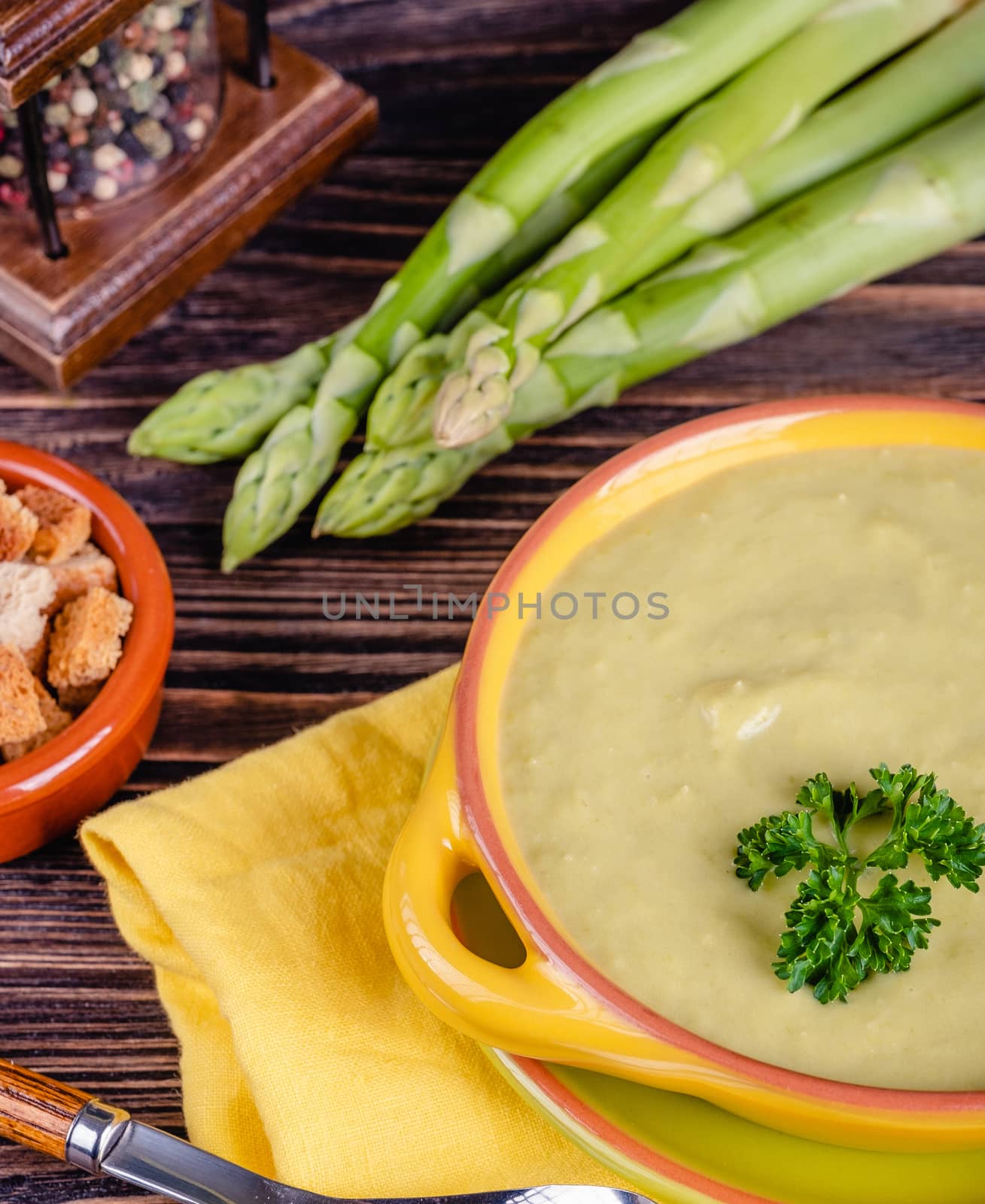 Fresh asparagus creamy soup and ingredients on wooden table on rustic wooden background, selective focus