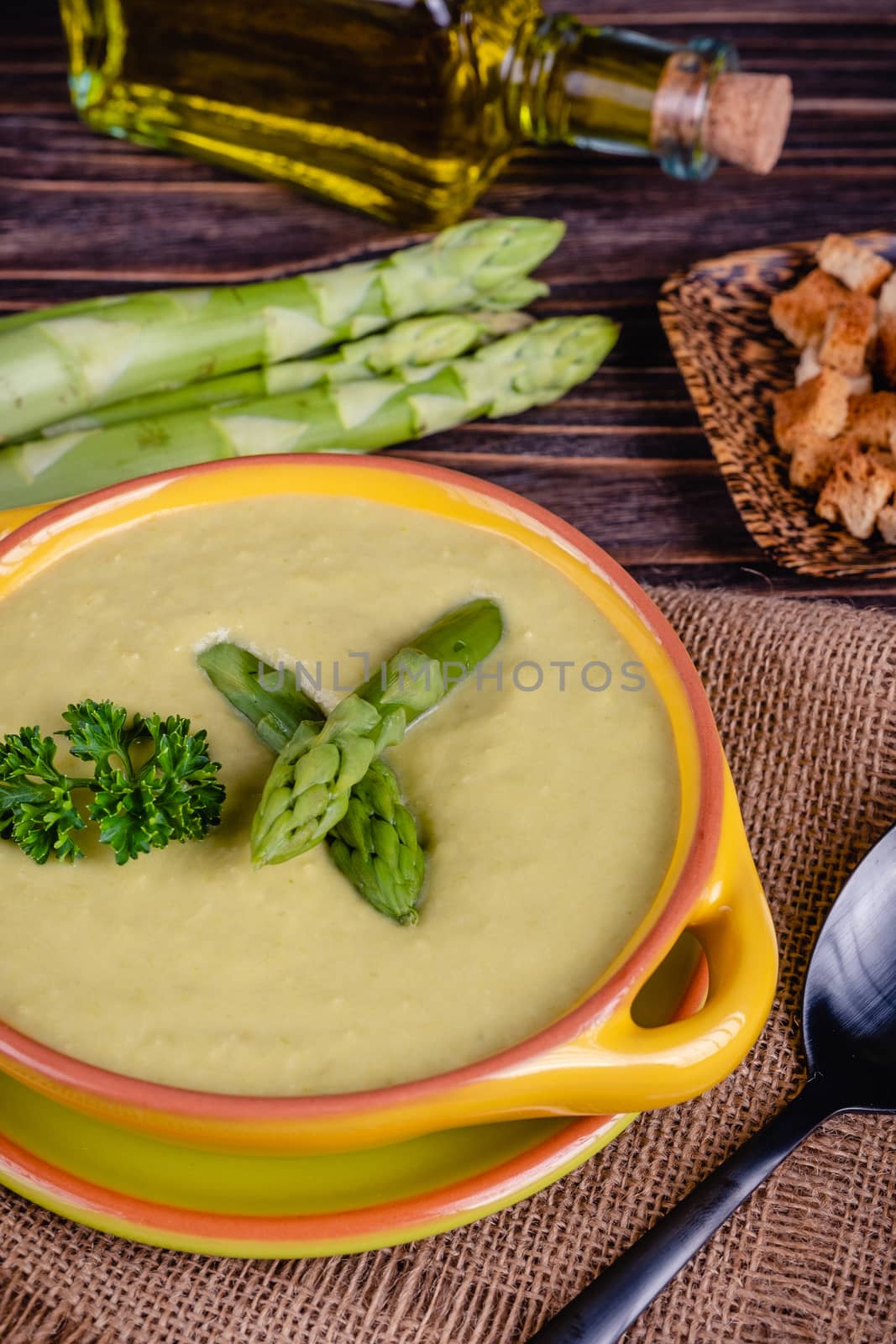 Fresh asparagus creamy soup and ingredients on wooden table on rustic wooden background, selective focus