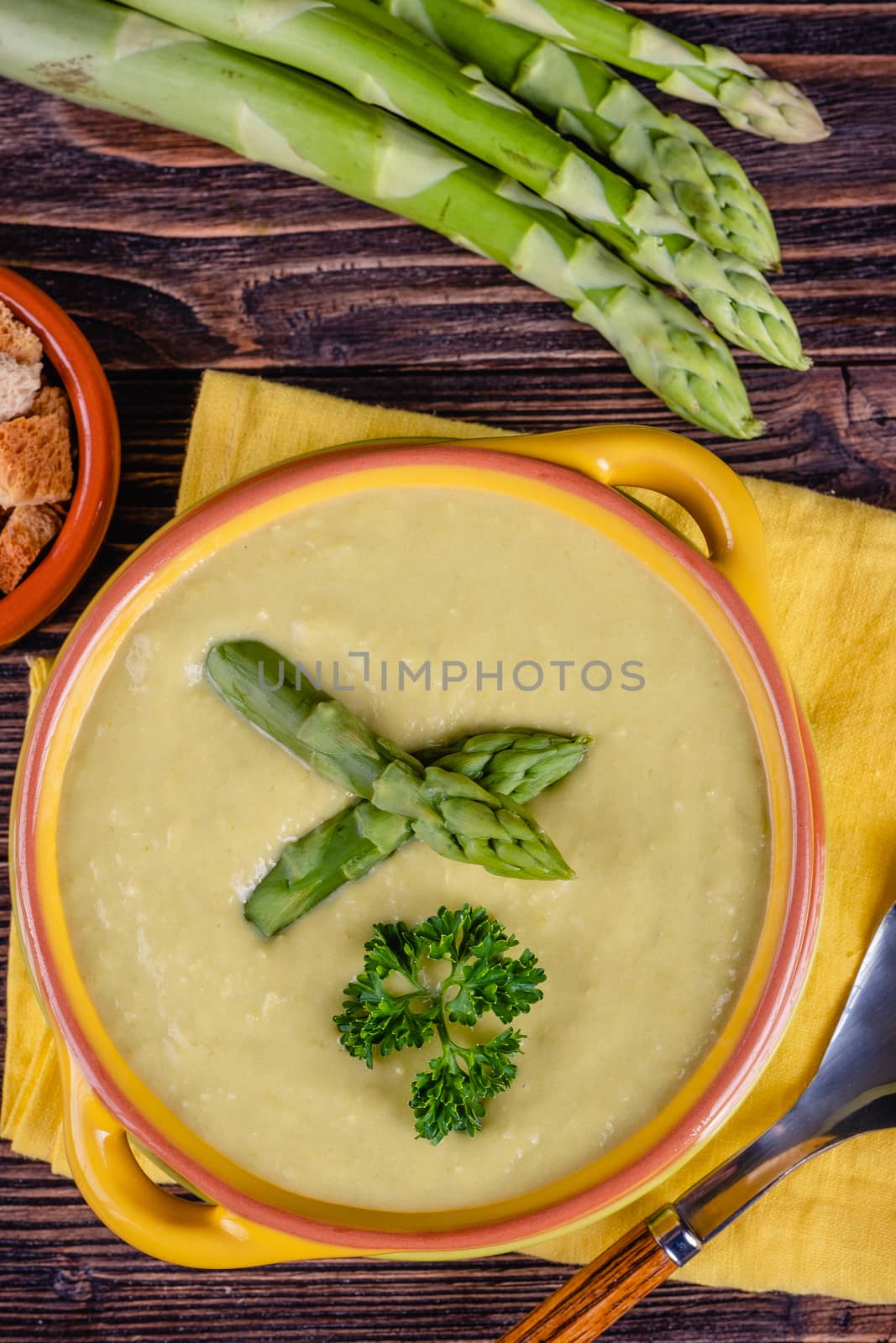 Fresh asparagus creamy soup and ingredients on wooden table on rustic wooden background, selective focus