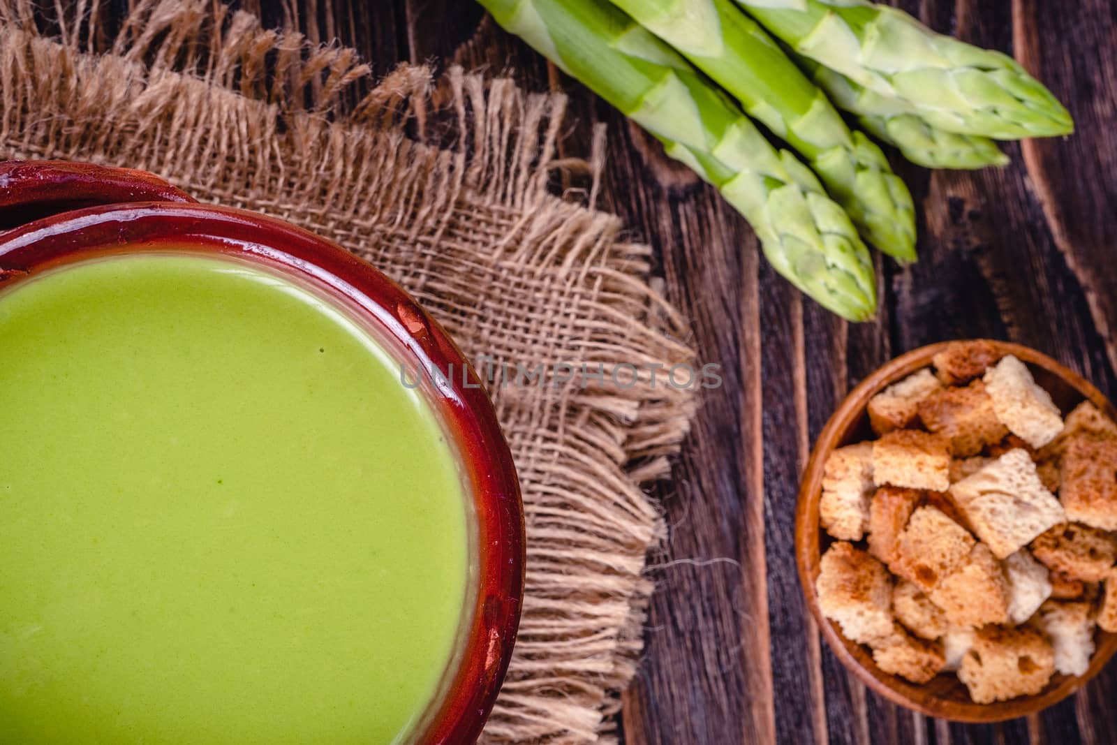 Fresh asparagus creamy soup and ingredients on wooden table on rustic wooden background, selective focus