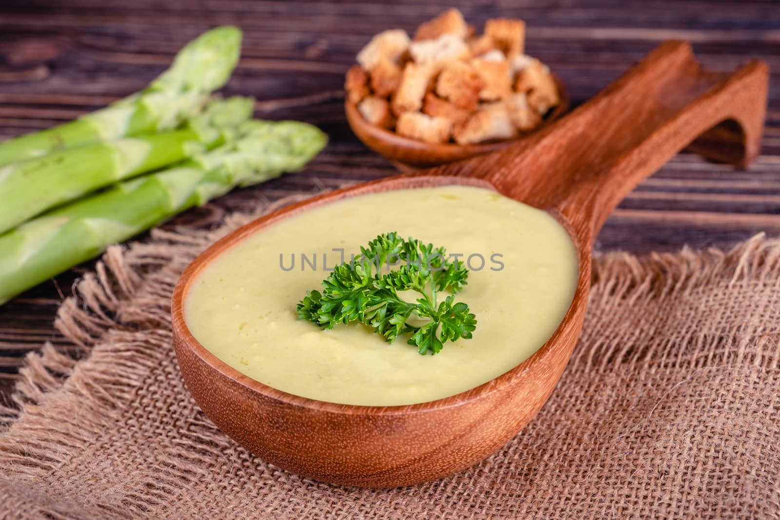 Fresh asparagus creamy soup and ingredients on wooden table on rustic wooden background, selective focus