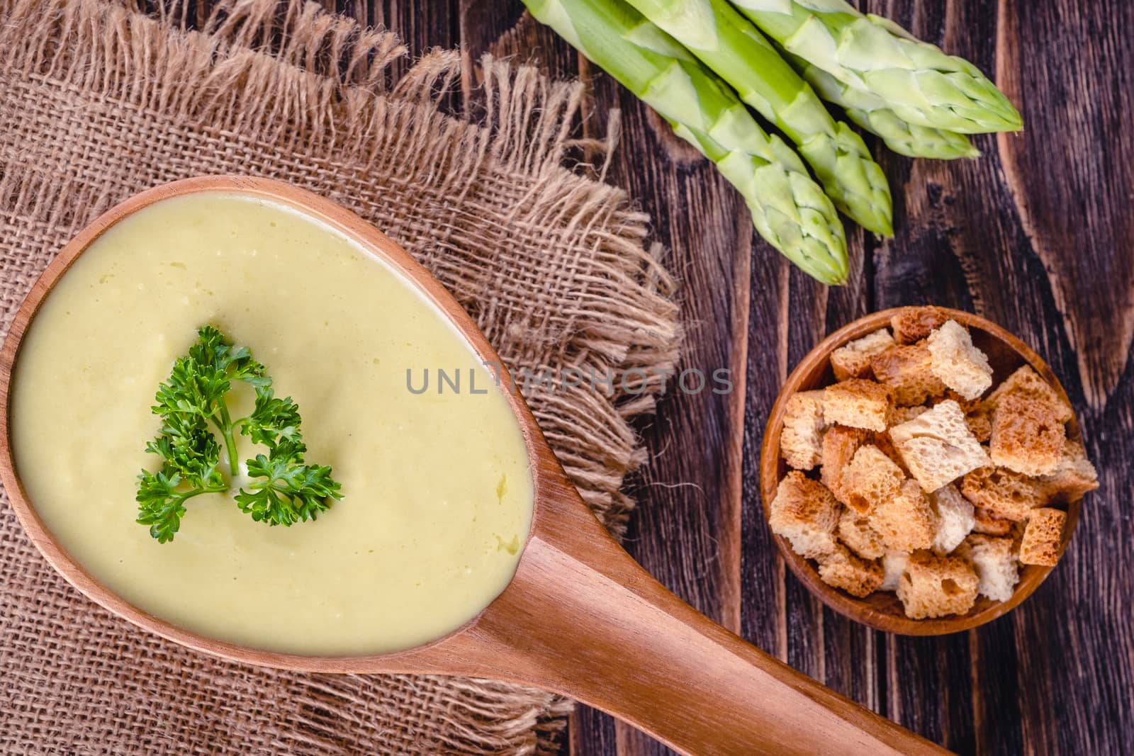 Fresh asparagus creamy soup and ingredients on wooden table on rustic wooden background, selective focus