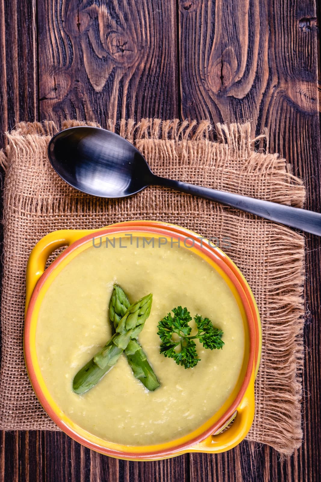 Fresh asparagus creamy soup and ingredients on wooden table on rustic wooden background, selective focus