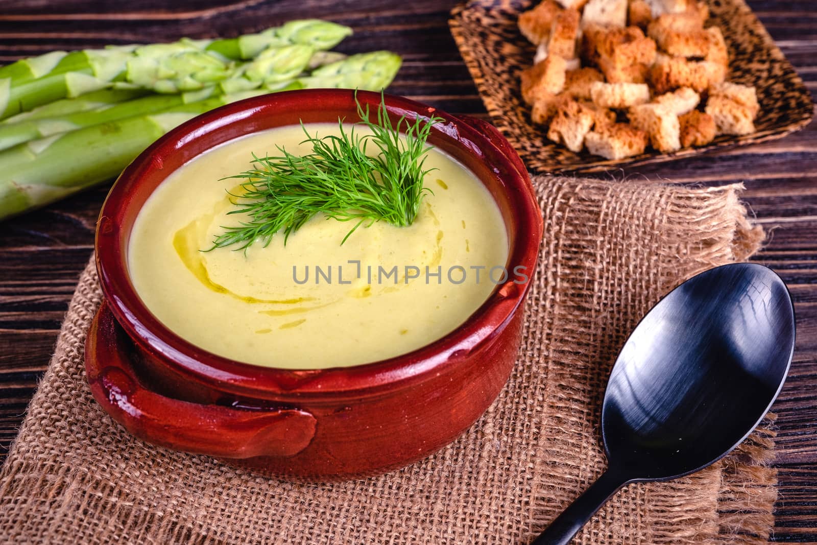 Fresh asparagus creamy soup and ingredients on wooden table on rustic wooden background, selective focus