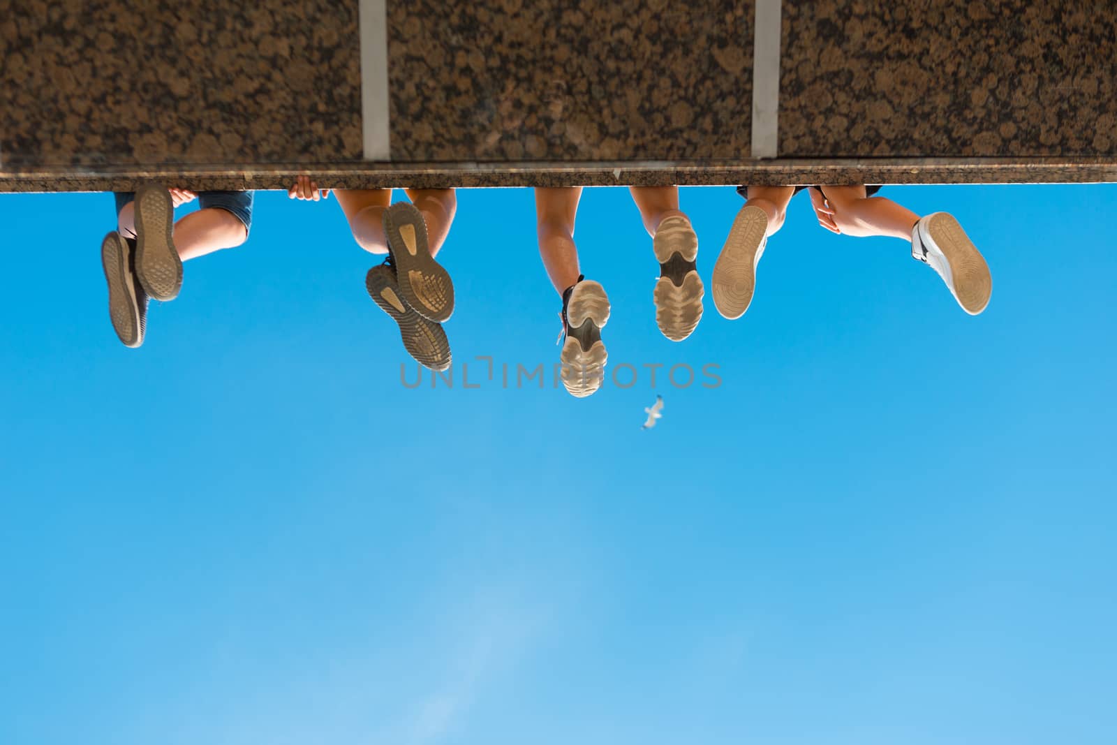 Boys legs in shoes hanging from the bridge against blue sky.