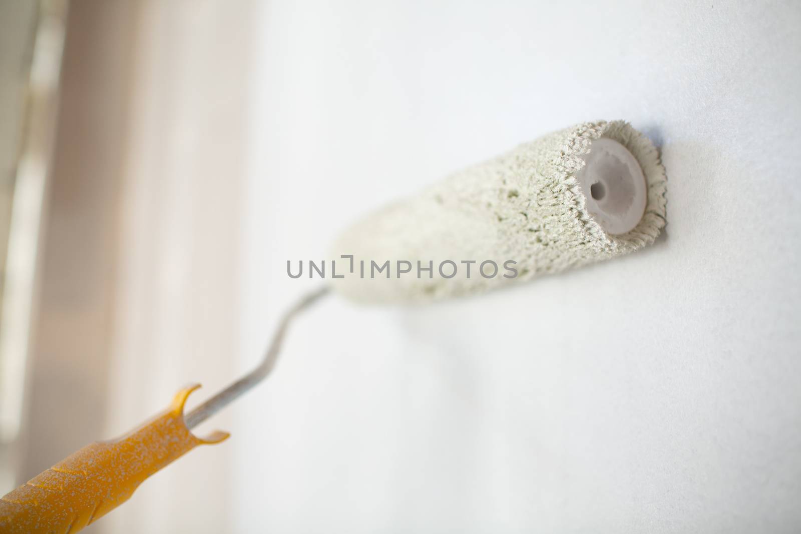 White paint roller in hand with drywall wall by primipil