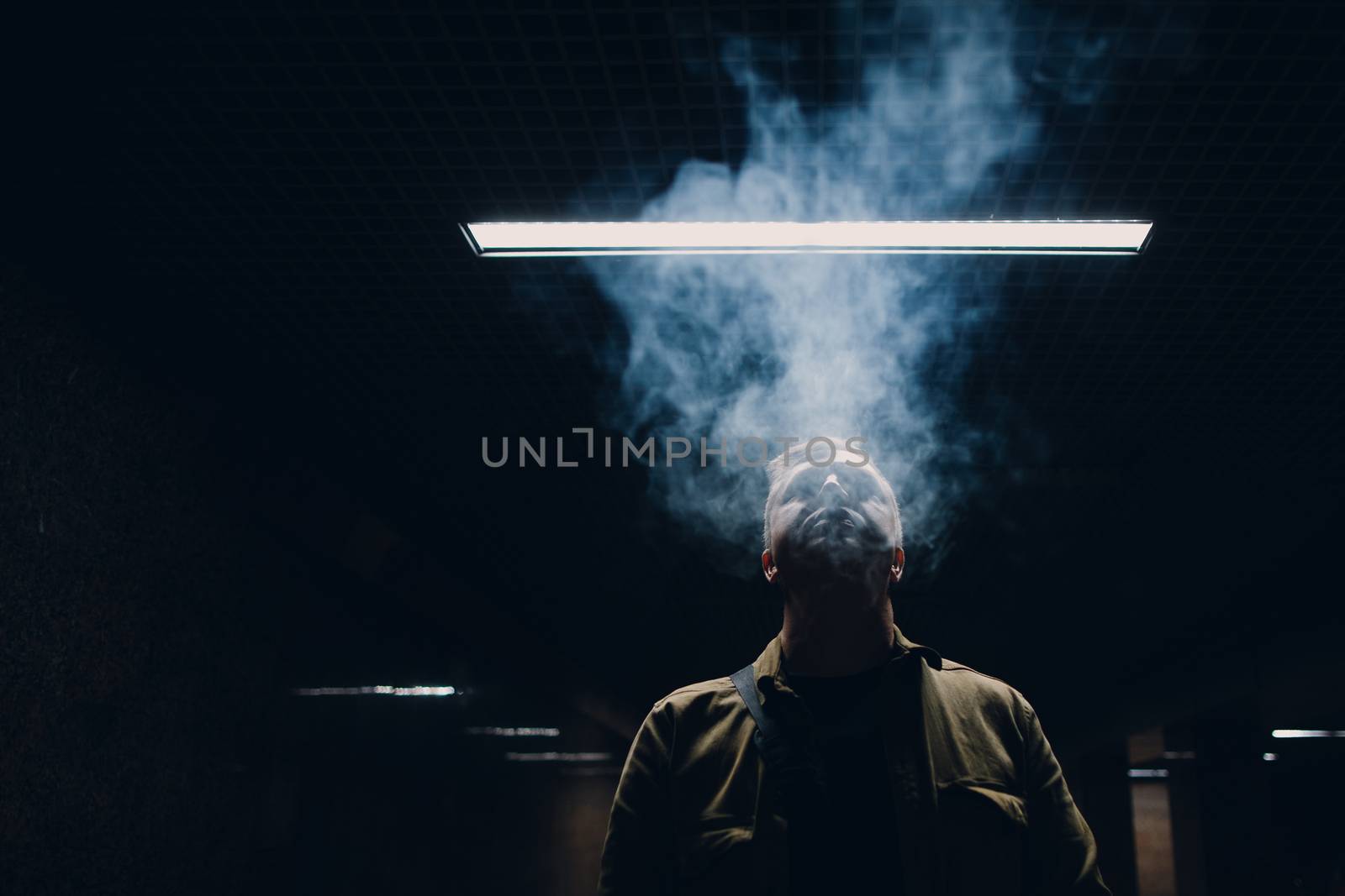 Portrait of young caucasian man smoking e-cigarette in dark with line light.