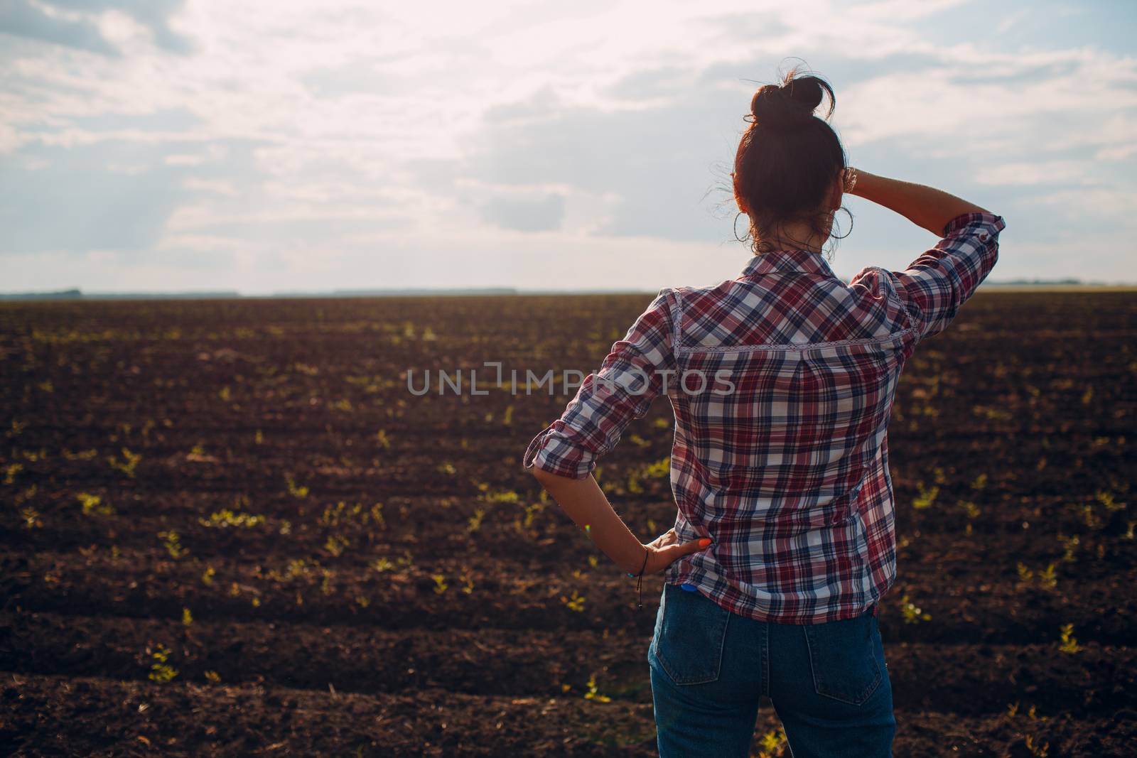 Woman farmer standing and looking agricultural field soil.