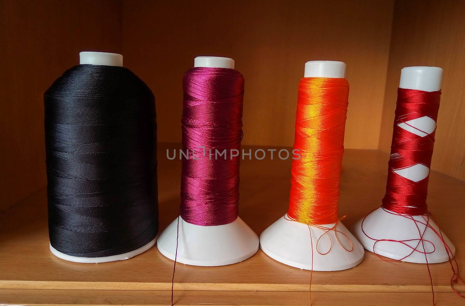 Multicolored sewing threads in bobbins stand on a brown shelf