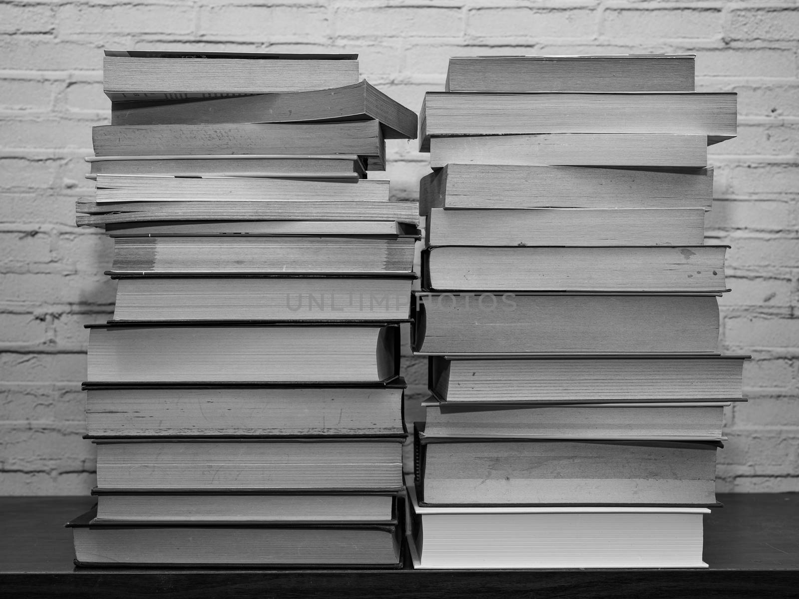 Black and white image of some books stacked on a shelf, light brick background